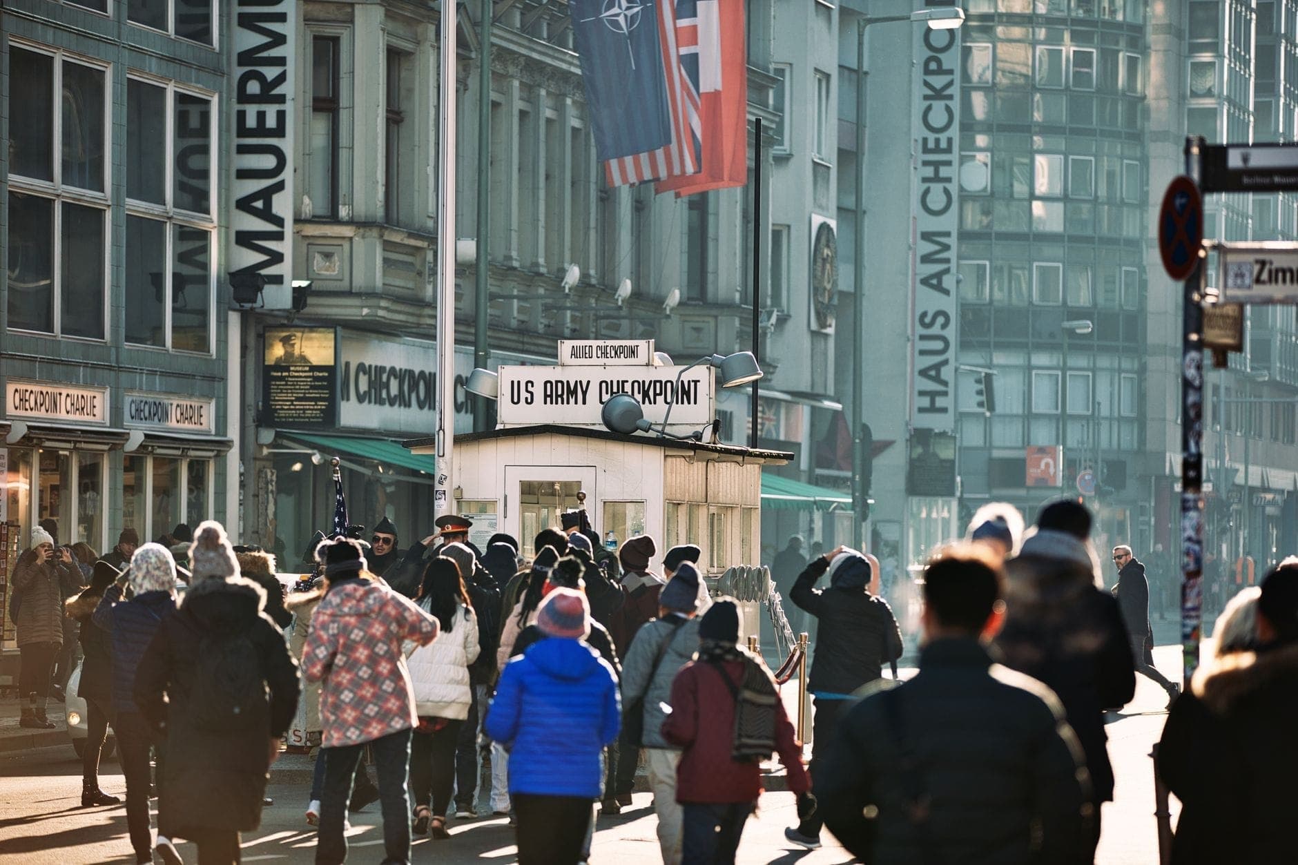 บรรยากาศคึกคักที่ Checkpoint Charlie ในกรุงเบอร์ลิน พร้อมฝูงชนนักท่องเที่ยว บ้านยามอันโด่งดัง และพิพิธภัณฑ์กำแพงเบอร์ลินโดยรอบ