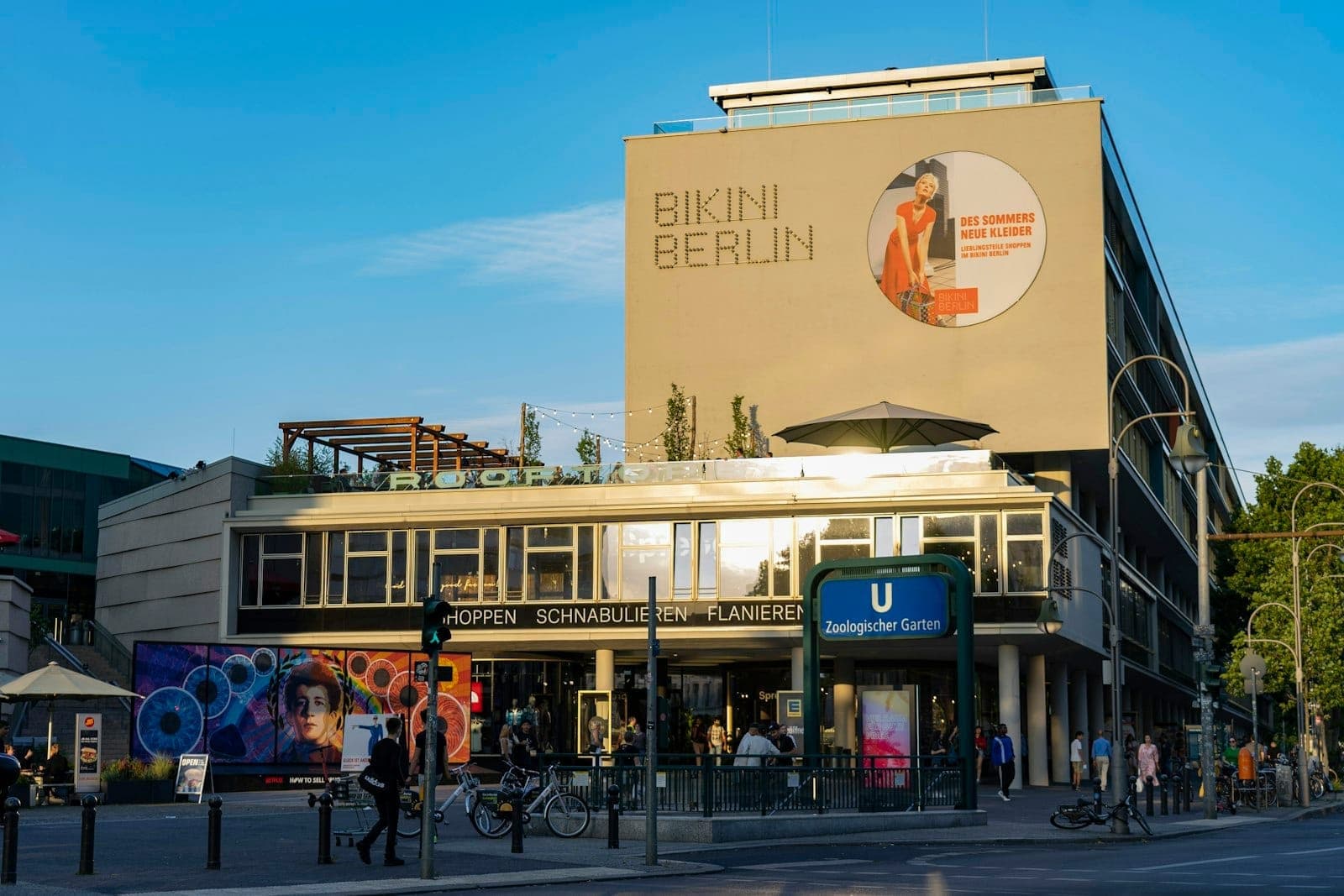 อาคารทันสมัยป้าย 'Bikini Berlin' คนเดินและปั่นจักรยาน หน้าสถานีรถไฟ U-Bahn ท้องฟ้าใส บรรยากาศเบอร์ลินสดใส