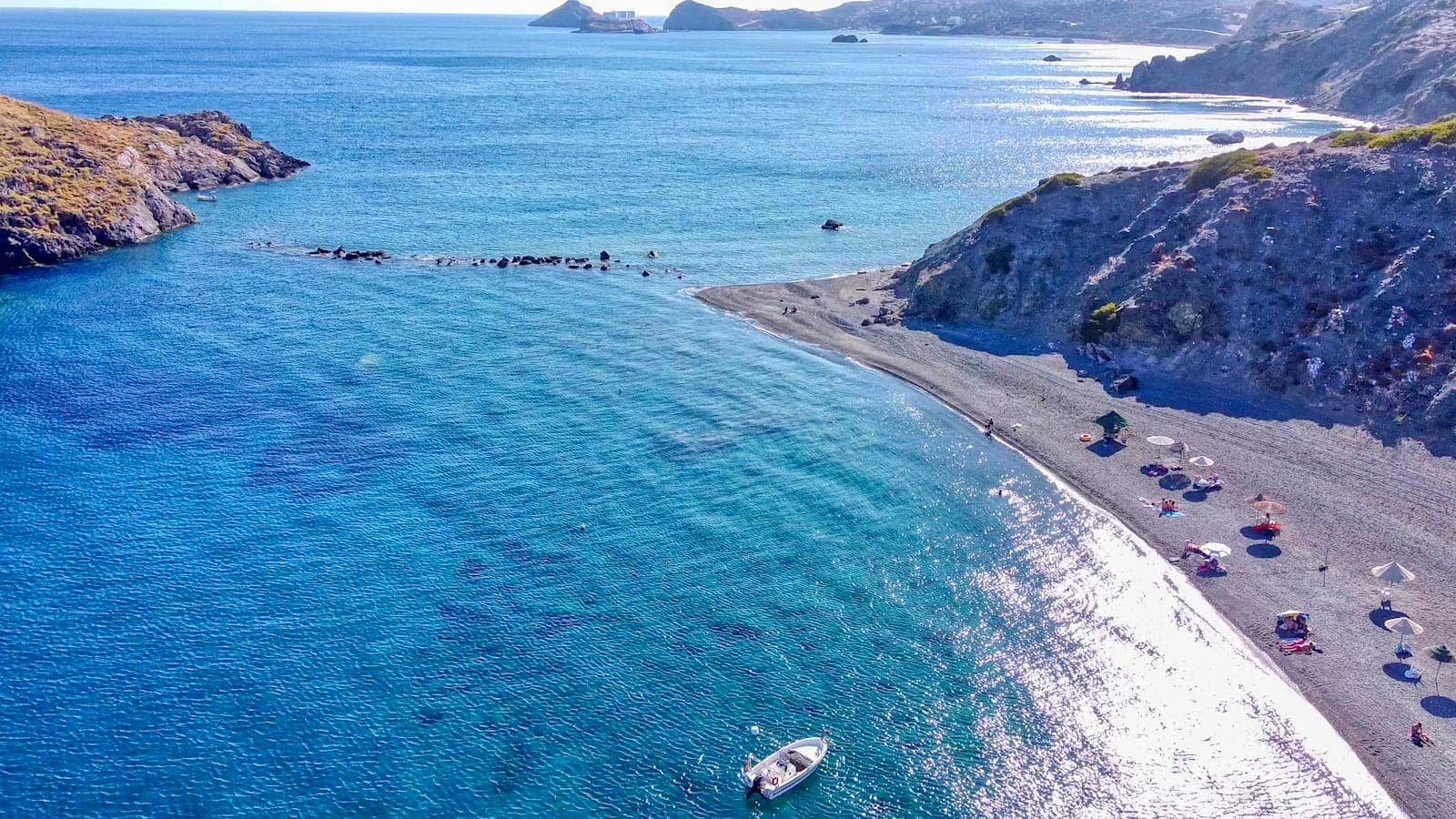 Una spettacolare spiaggia rocciosa sulla costa meridionale di Creta, con acque turchesi, pochi ombrelloni e scogliere frastagliate sullo sfondo.