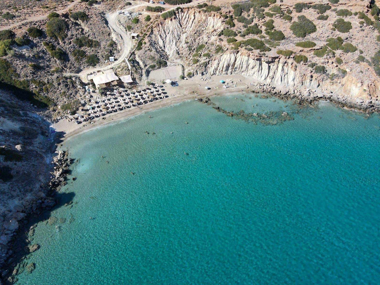Una spiaggia rocciosa e isolata a Creta con acqua turchese, lettini, ombrelloni e scogliere frastagliate sullo sfondo.