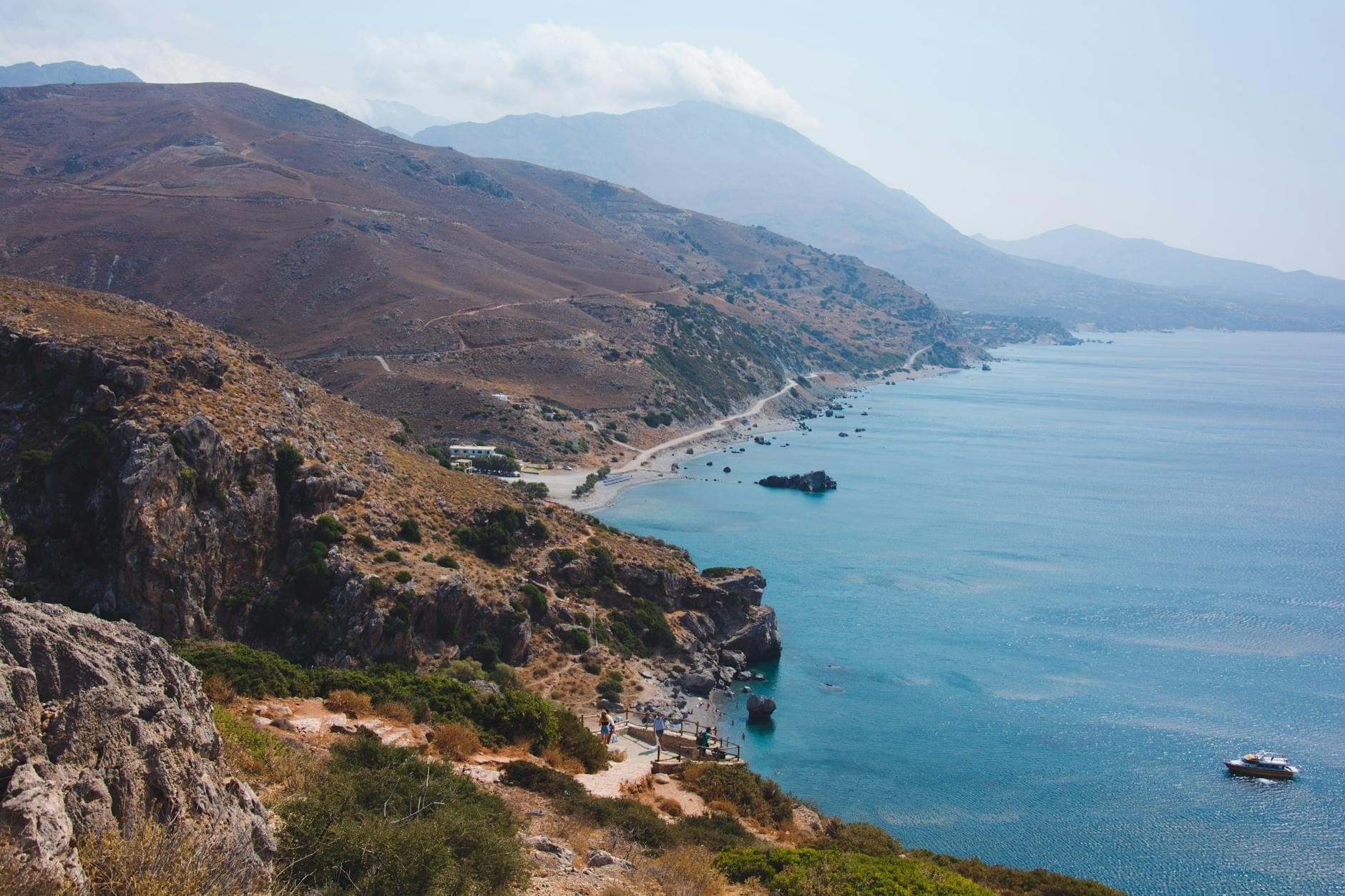 Ripide scogliere rocciose che si affacciano su una costa incontaminata con acque turchesi e alcuni edifici sparsi, che catturano la bellezza selvaggia del Creta meridionale.