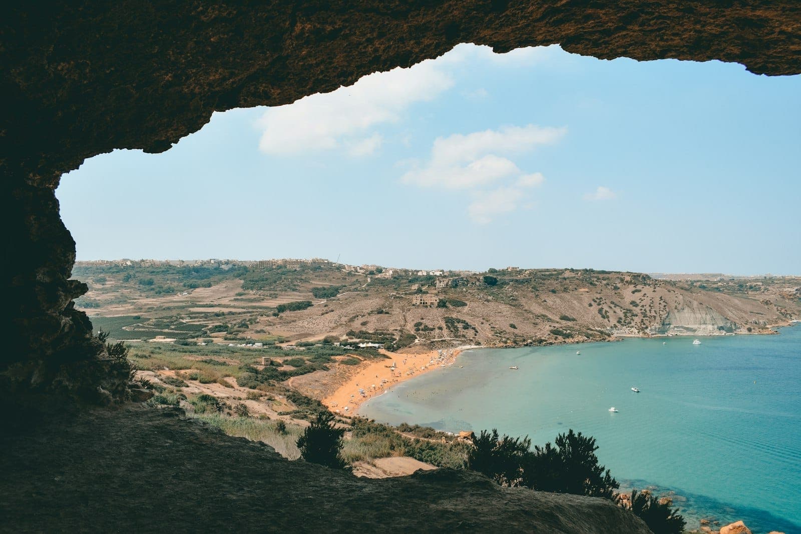 Strandblick aus einer Höhle mit goldenem Sand, klarem blauem Wasser und zerklüfteten Klippen auf Gozo, Malta