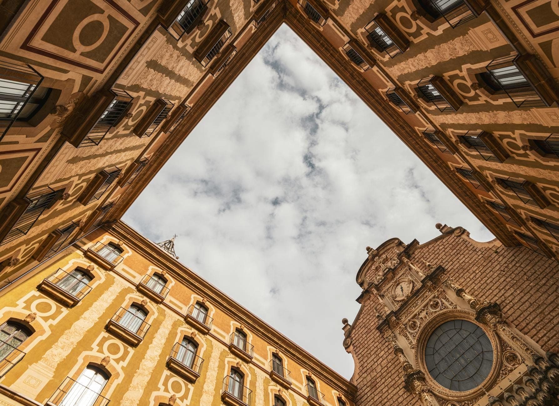 Fachada de igreja barroca em Nápoles emoldurada por edifícios ocres ricamente decorados sob um céu nublado, vista de um dramático ângulo ascendente.