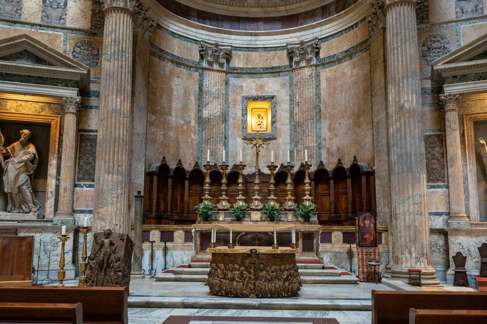 O altar no interior do Pantheon em Roma, com antigas colunas de mármore, um altar ornamentado, obras de arte religiosas e arquitetura clássica romana.