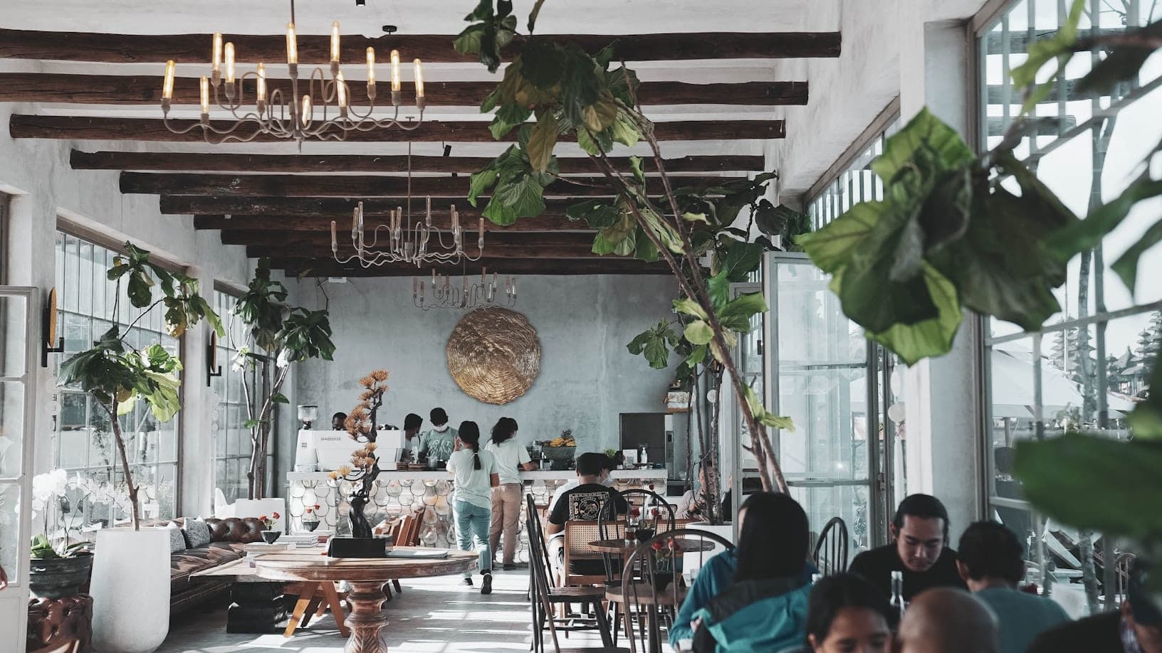 Busy cafe interior in Bali with travelers dining and tropical plants inside a modern restaurant