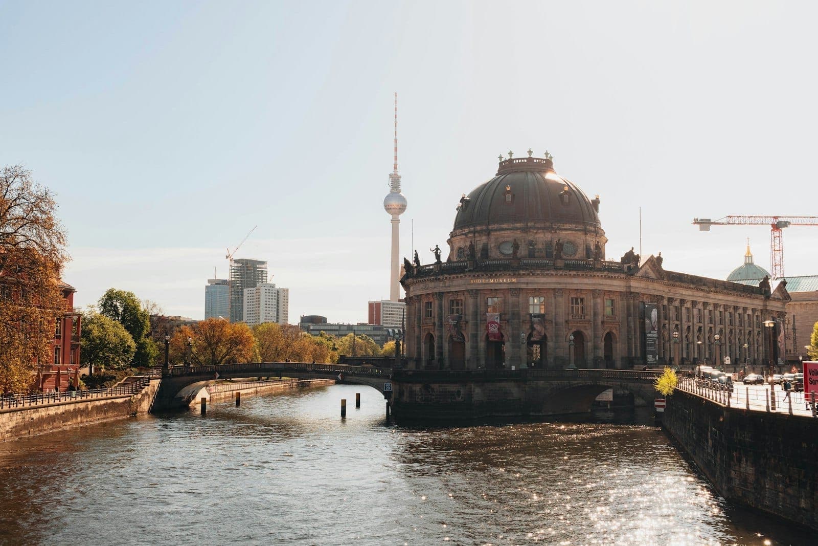 Bode Museum na berlińskiej Wyspie Muzeów, z rzeką Sprewą, drzewami, łodzią wycieczkową i berlińską wieżą telewizyjną w tle.