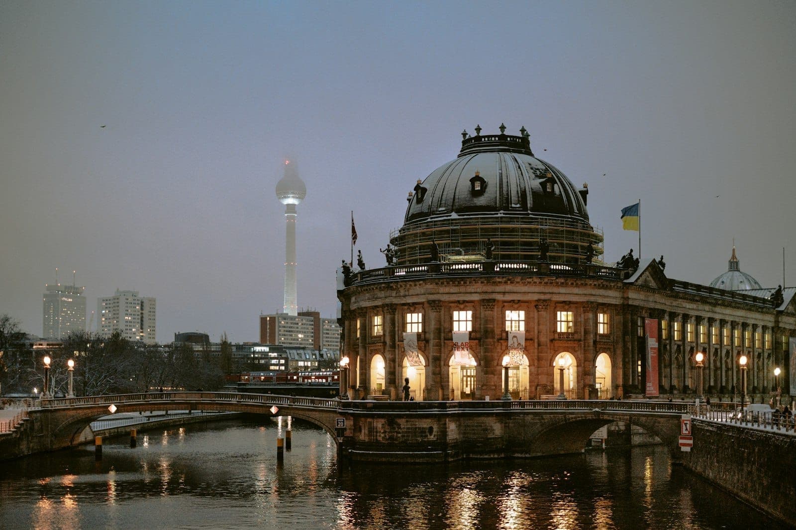 Wieczorny widok na Bode Museum w Berlinie nad rzeką Spree, z wieżą telewizyjną w tle.