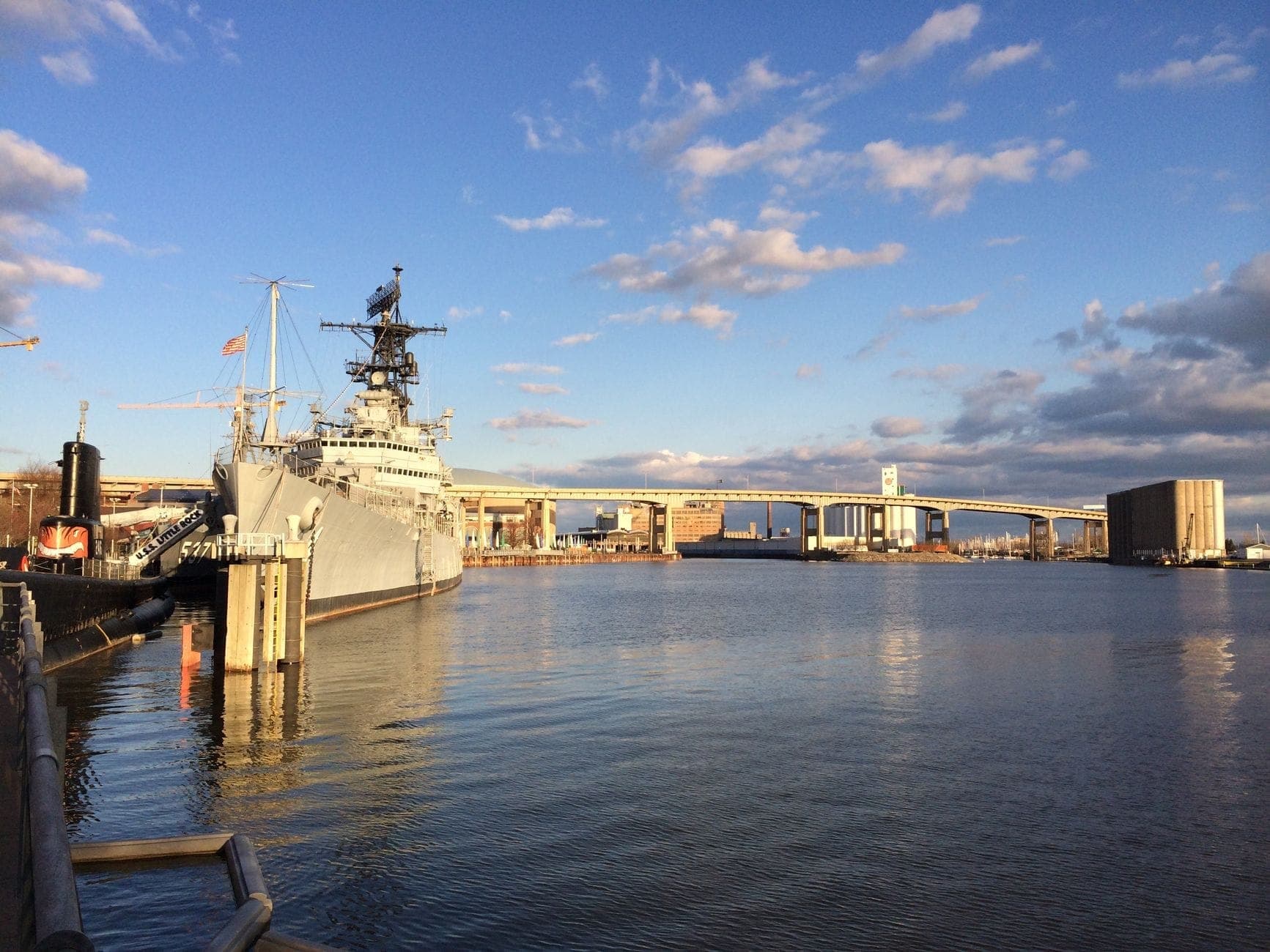 Destroyer naval désarmé amarré le long du front de mer de Boston sous un ciel partiellement nuageux, avec des bâtiments et des ponts en arrière-plan.