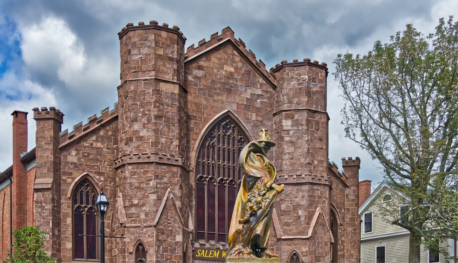 Vue extérieure d'un musée en pierre de style gothique à Salem avec une statue d'un personnage devant et des arbres à proximité.