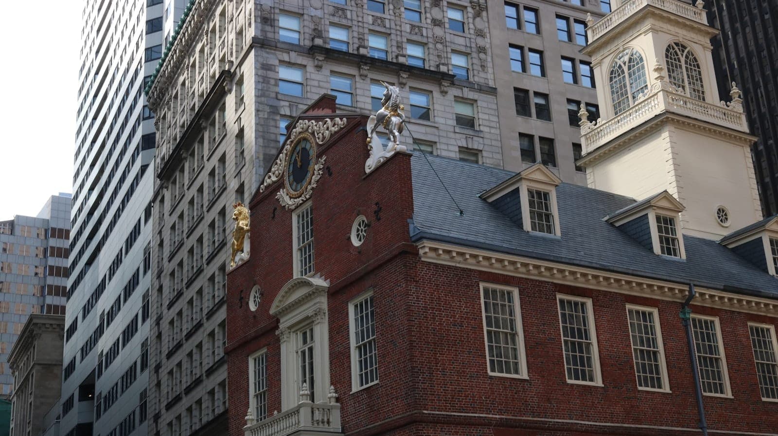 L'historique bâtiment en brique et garnitures blanches de l'Old State House entouré de gratte-ciel modernes dans le centre-ville de Boston, vu depuis le niveau de la rue.