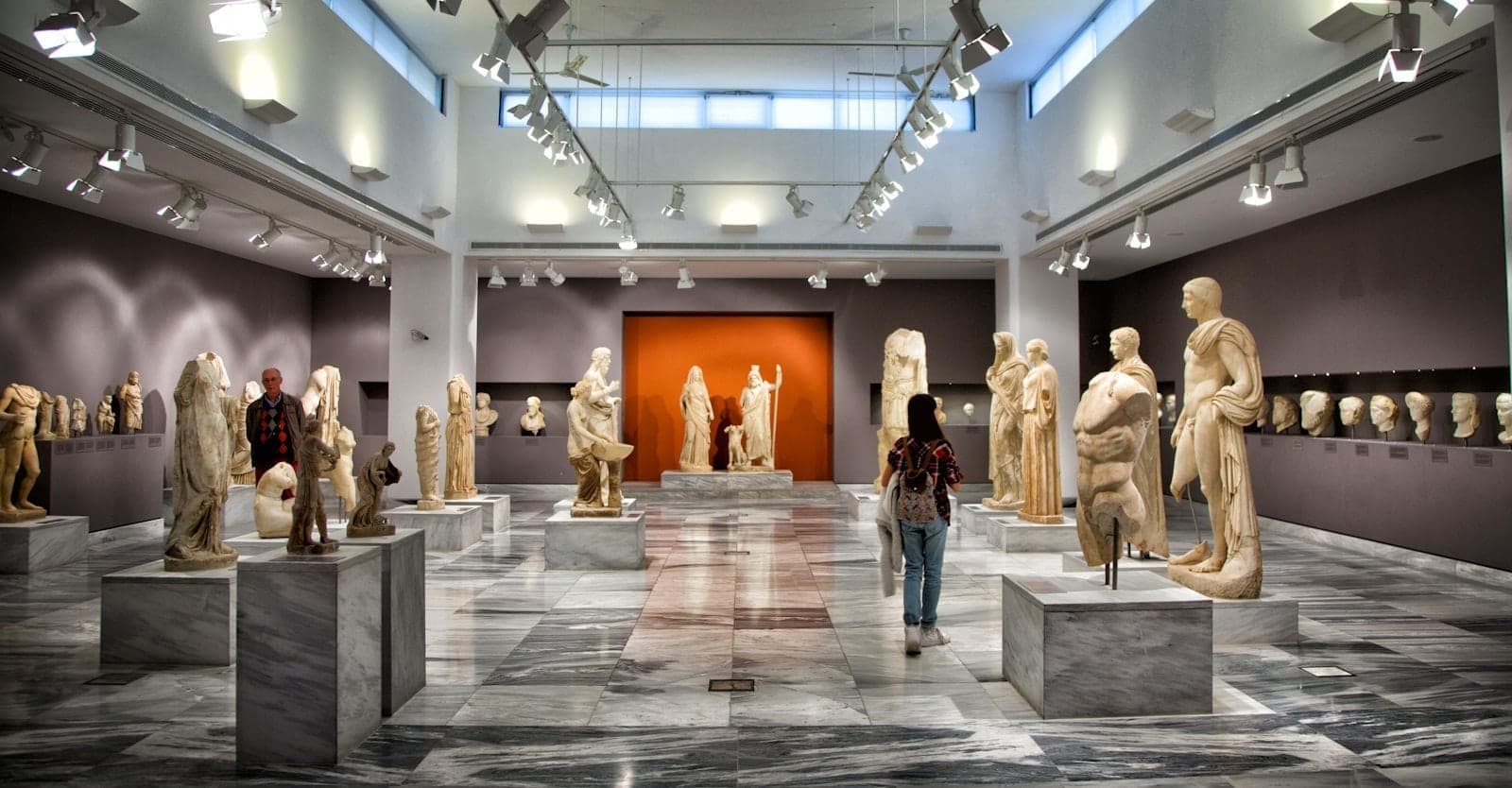 Interno di una galleria museale ben illuminata a Creta con antiche statue di marmo greche e romane in mostra e visitatori che esplorano le esposizioni.