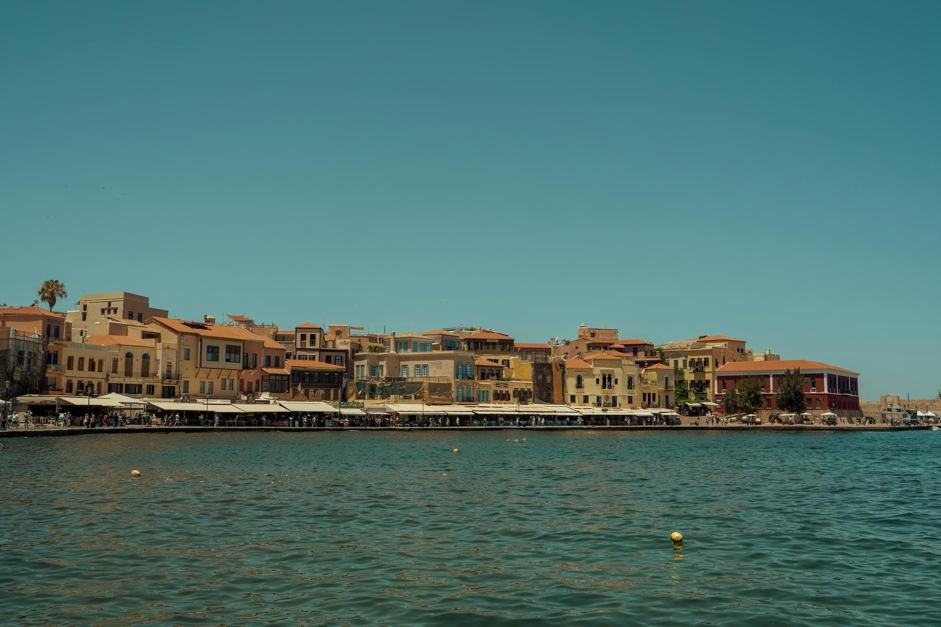 Vista del lungomare del centro storico di Chania, Creta, con colorati edifici storici veneziani lungo il porto sotto un cielo azzurro limpido.
