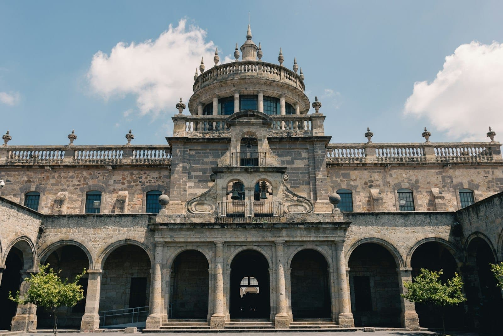 มุมมองด้านหน้าของ Hospicio Cabañas ในกวาดาลาฮารา ในวันที่แดดจ้า โดดเด่นด้วยสถาปัตยกรรมประวัติศาสตร์แบบสมมาตร ทางเข้าโค้ง และท้องฟ้าสีฟ้า