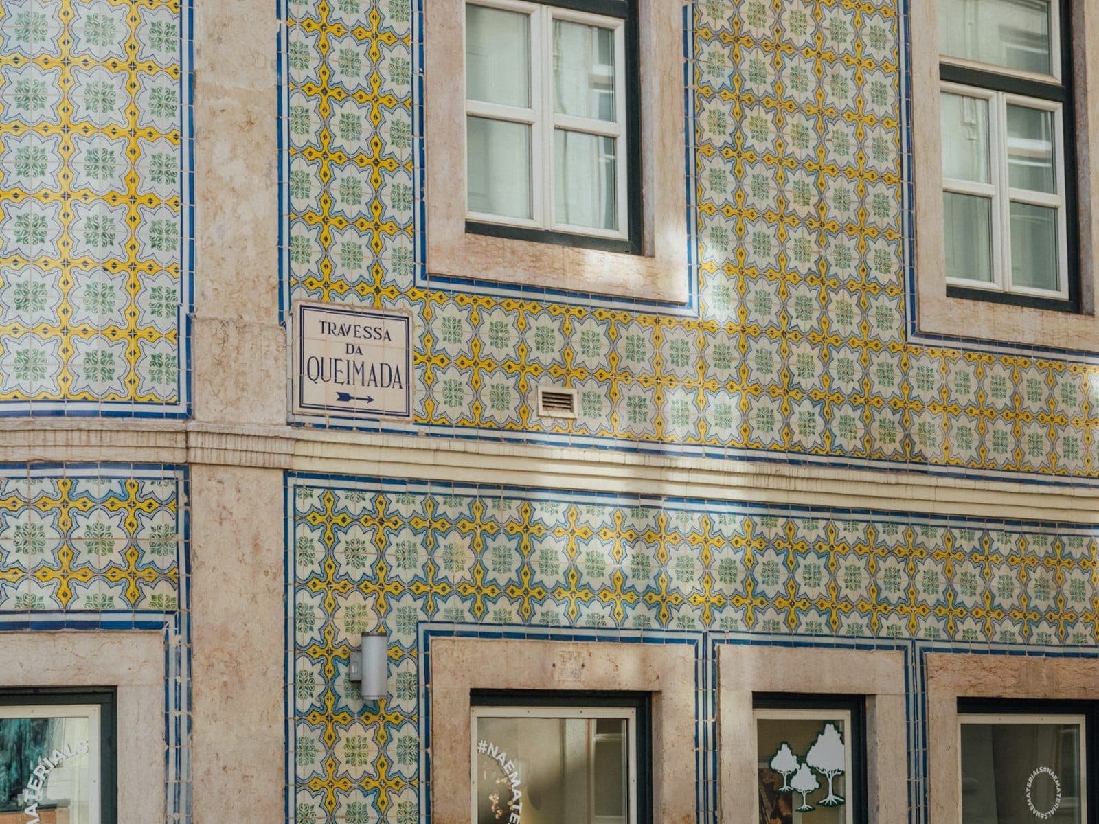 Esquina de rua em Lisboa coberta de azulejos tradicionais, mostrando janelas e placa com o nome do edifício à luz do dia