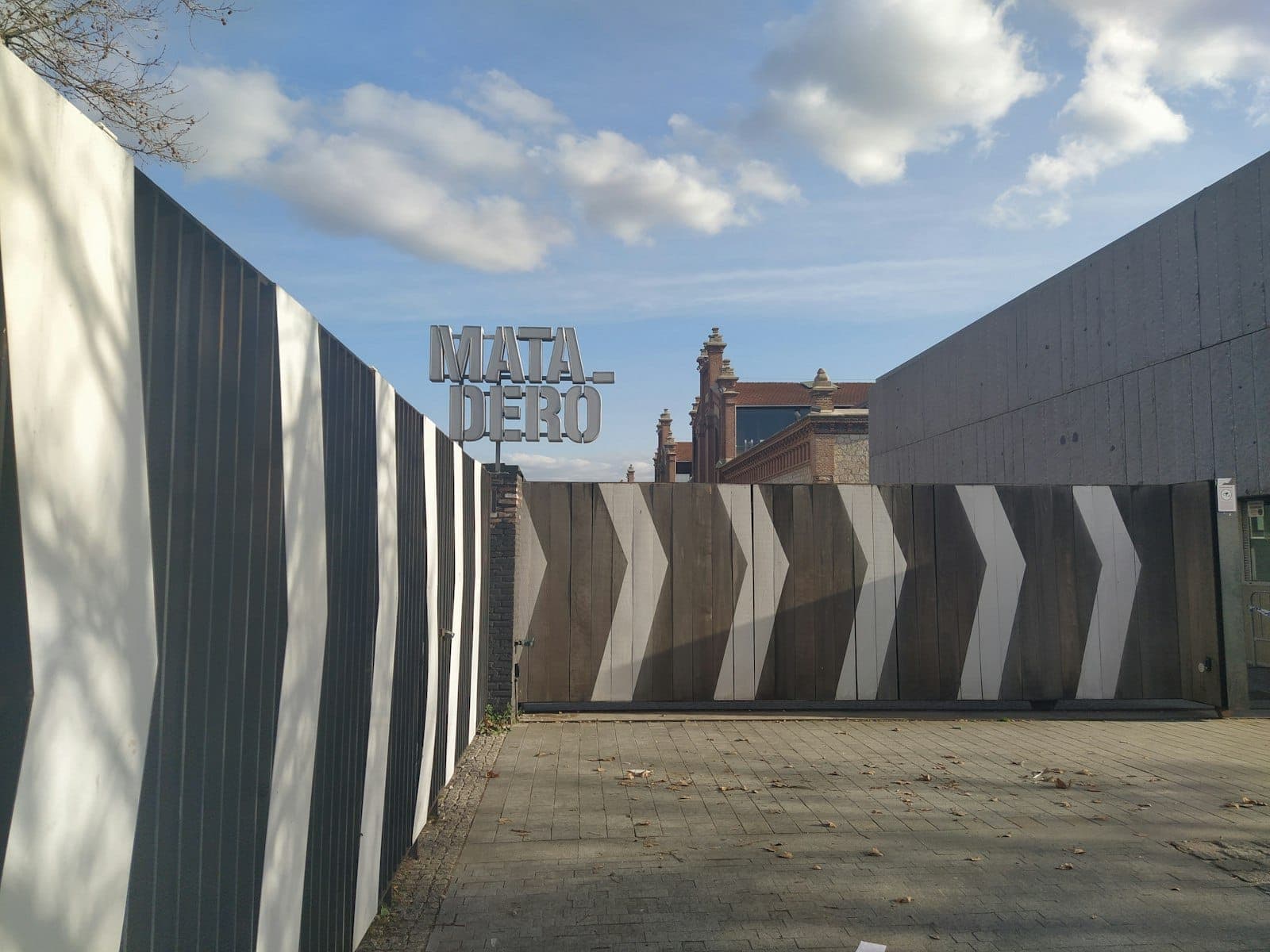 Brama wejściowa Matadero Madrid z wyraźnym szyldem i nowoczesnymi elementami graficznymi na tle błękitnego nieba.