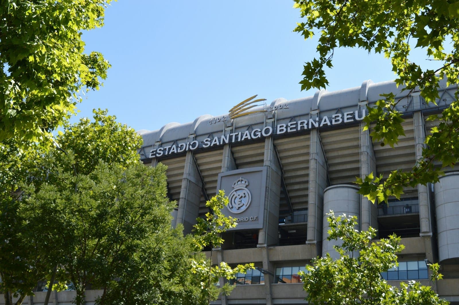 Widok zewnętrzny stadionu Estadio Santiago Bernabéu w Madrycie otoczonego zielonymi drzewami w słoneczny i pogodny dzień