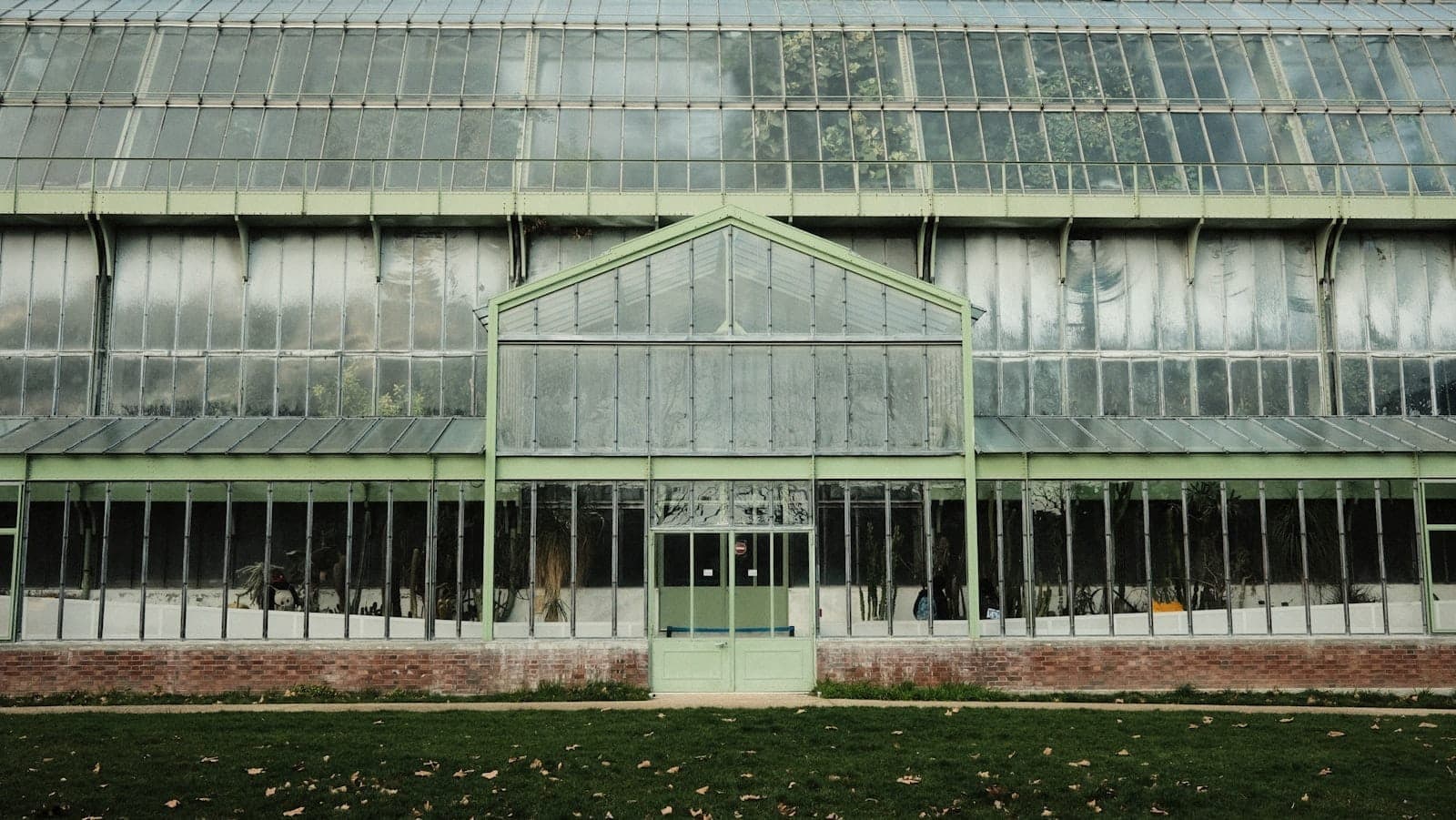 Harapan ng isang malaking greenhouse na salamin na may berdeng damuhan sa harap, bahagi ng Jardin des Plantes sa Paris.