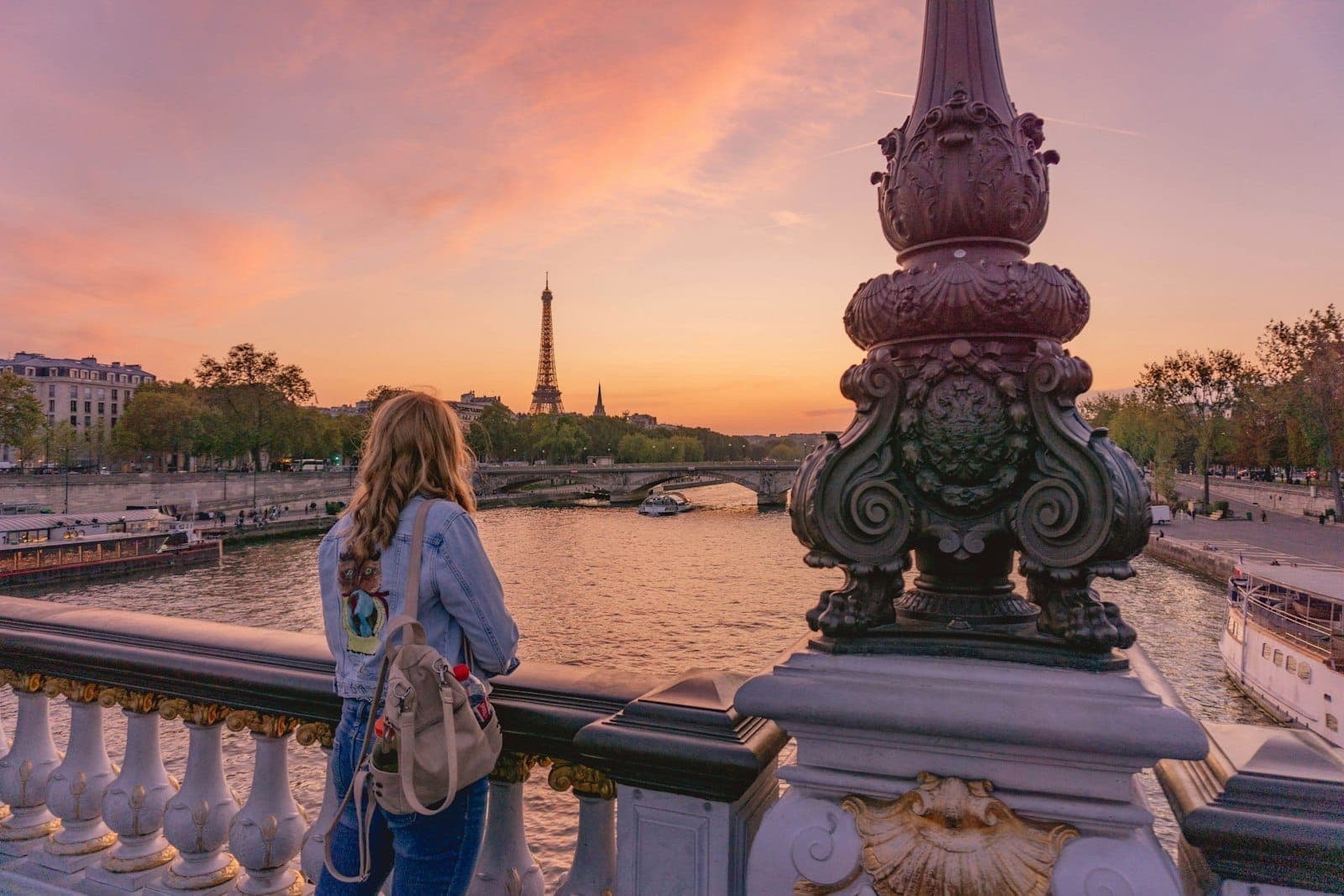 Wanita di jembatan Paris yang indah saat matahari terbenam dengan pemandangan Sungai Seine, Menara Eiffel di latar belakang, dan tiang lampu dekoratif.