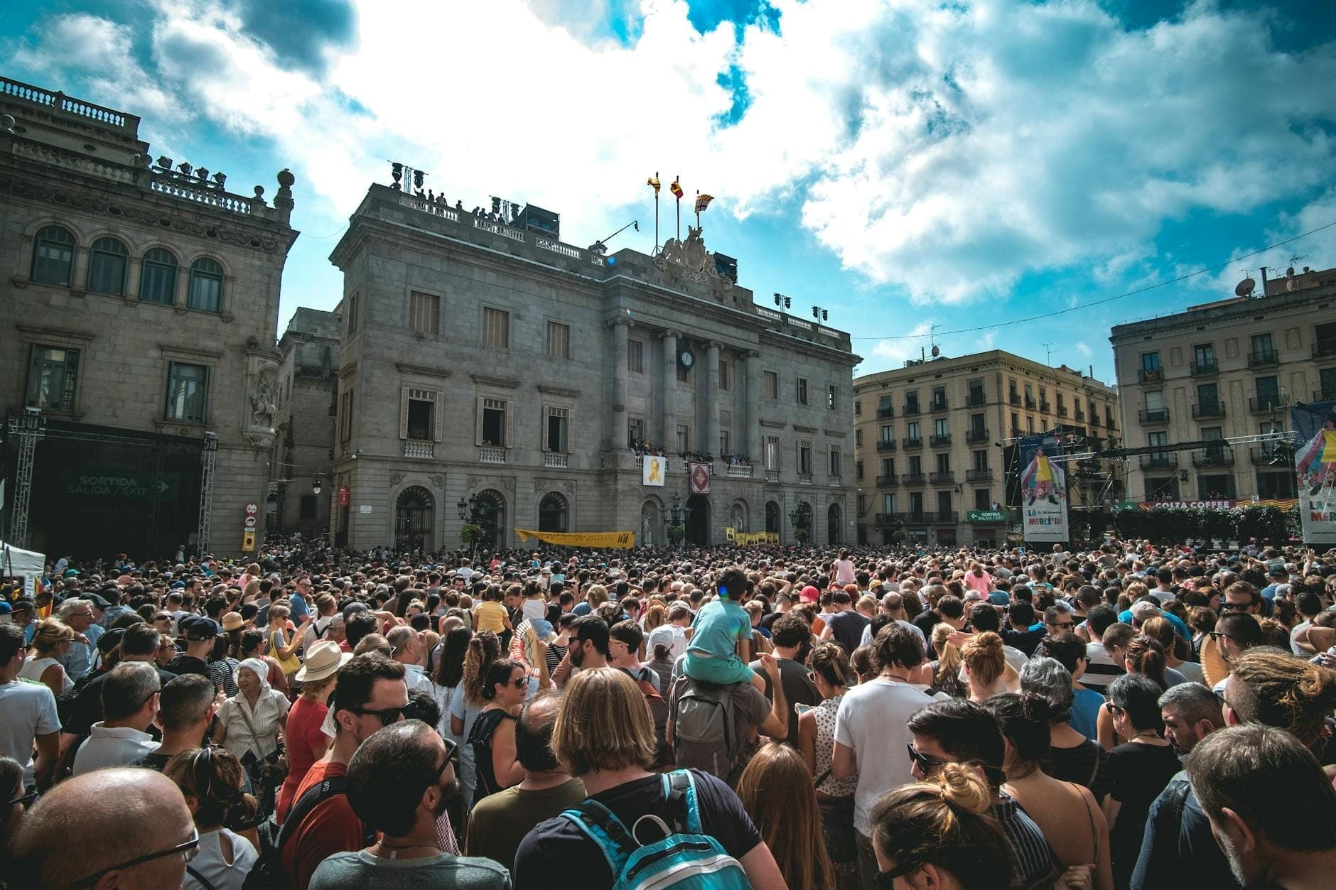 Large crowd gathered in Plaça de Sant Jaume, Barcelona, in front of historic buildings during a daytime festival in clear weather.