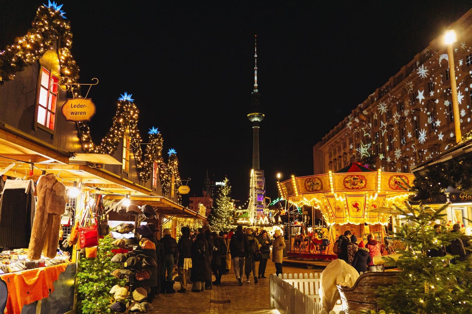 Mercado navideño de Berlín de noche con luces festivas, puestos decorados, un carrusel y el Fernsehturm al fondo
