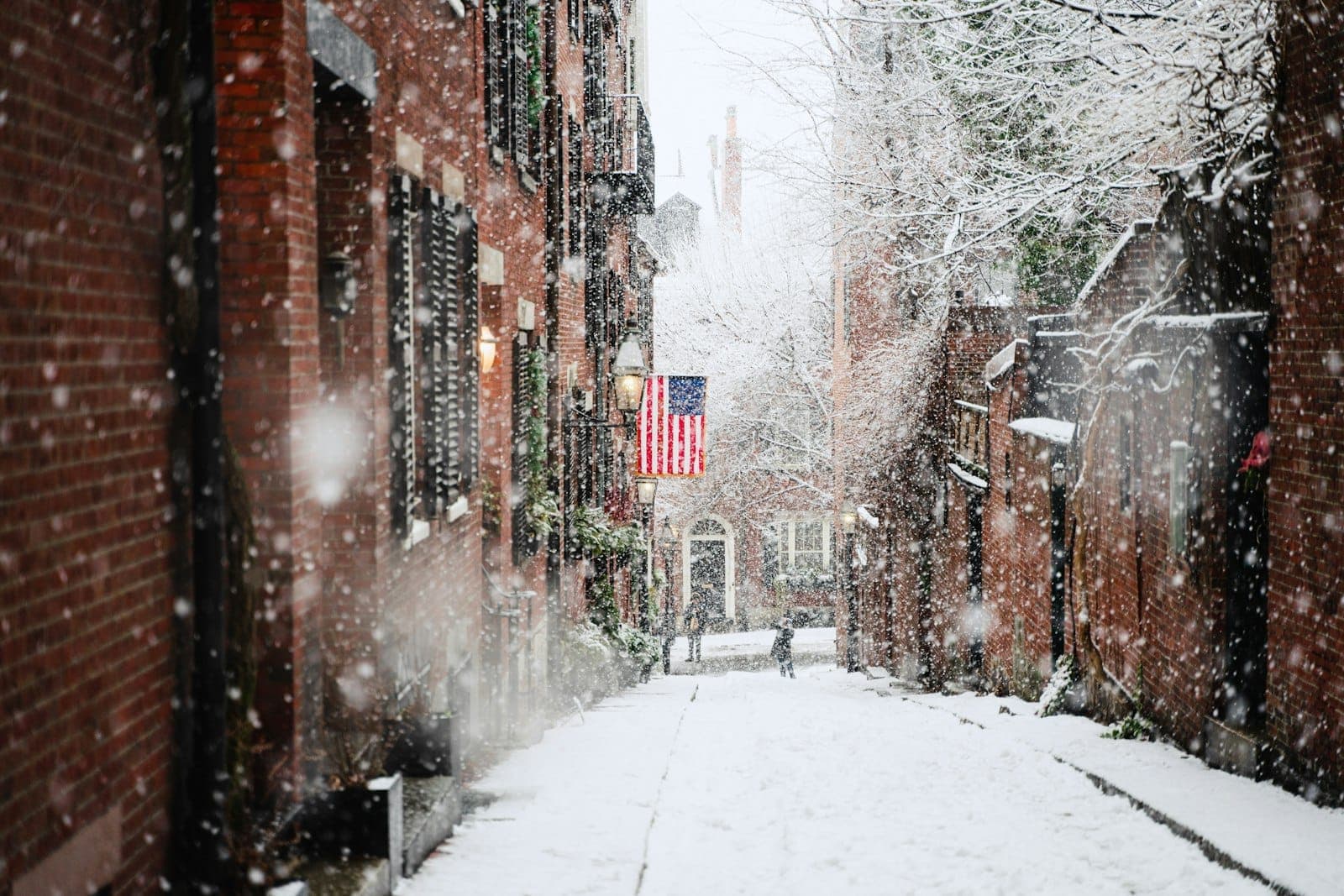 Une rue enneigée de Boston bordée de bâtiments en brique et d'un drapeau américain, avec une neige tombant abondamment en hiver.