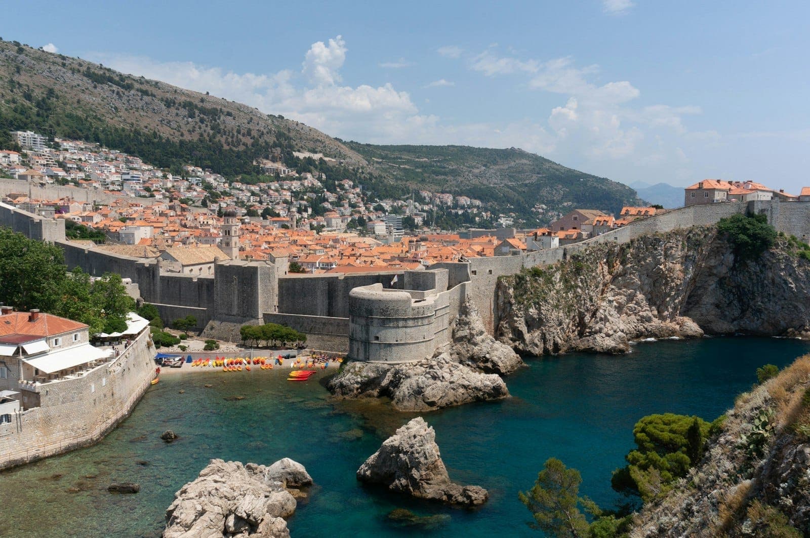 Dubrovnik Eski Şehir surlarının denizin üzerinde yükseldiği, turuncu çatıların ve çevre tepelerin açık gün ışığında göründüğü geniş bir manzara.