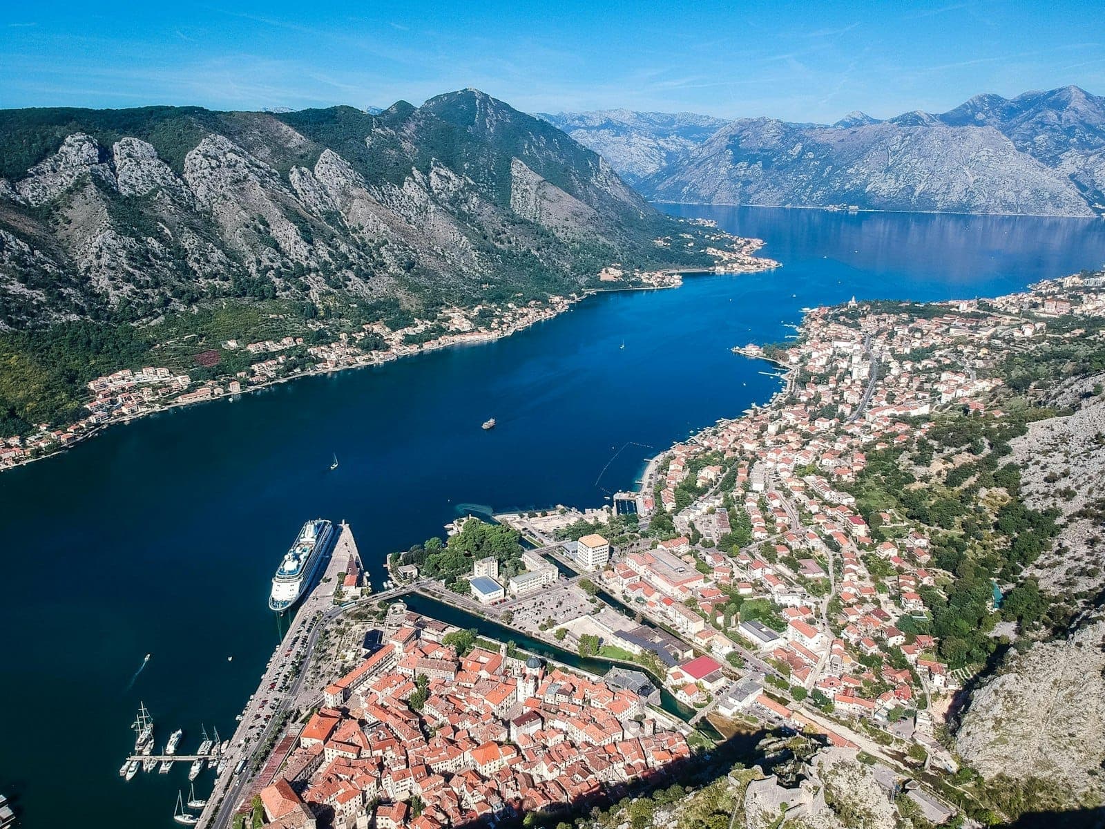 Vue aérienne de la baie de Kotor montrant un bateau de croisière, la vieille ville, les routes côtières et les montagnes, illustrant les principales voies d'arrivée et les options de déplacement local.