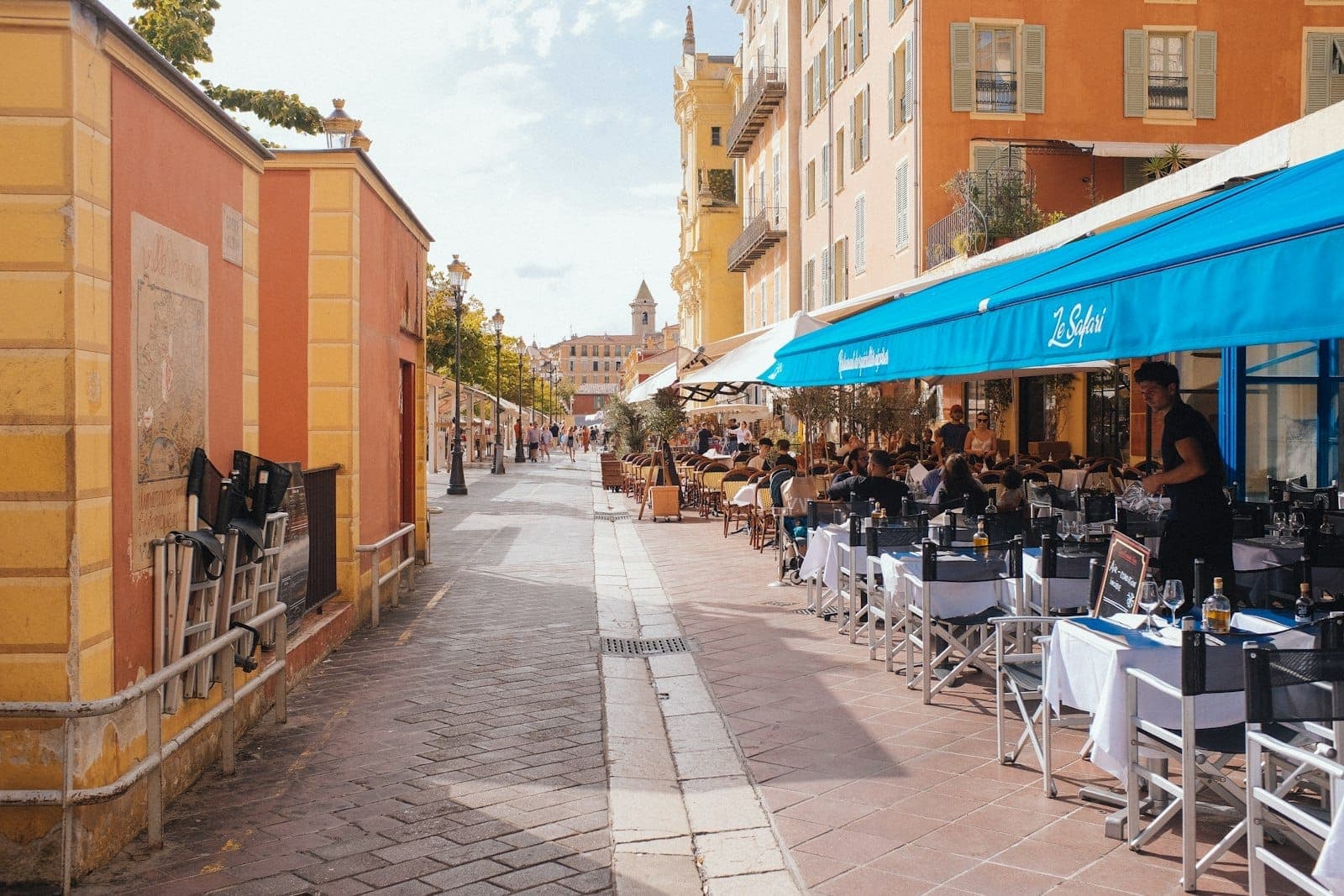 Pranzo all'aperto in un vivace ristorante di Mallorca con tenda blu, situato lungo una strada soleggiata fiancheggiata da colorati edifici mediterranei.