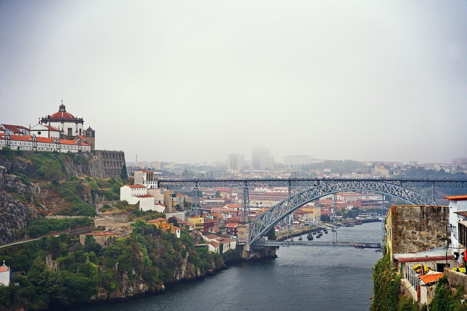 La niebla envuelve el horizonte de Oporto, con el río Duero, el icónico Puente Dom Luís I y los edificios en las laderas visibles bajo cielos nublados.