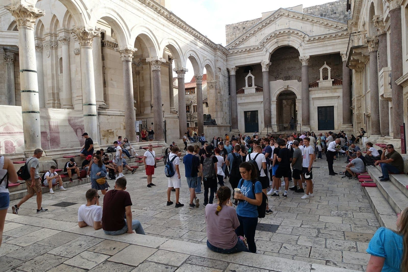 Una vivace folla estiva riempie il cortile del Peristilio del Palazzo di Diocleziano a Spalato, in Croazia, con persone sedute e in piedi tra l'antica architettura di marmo.