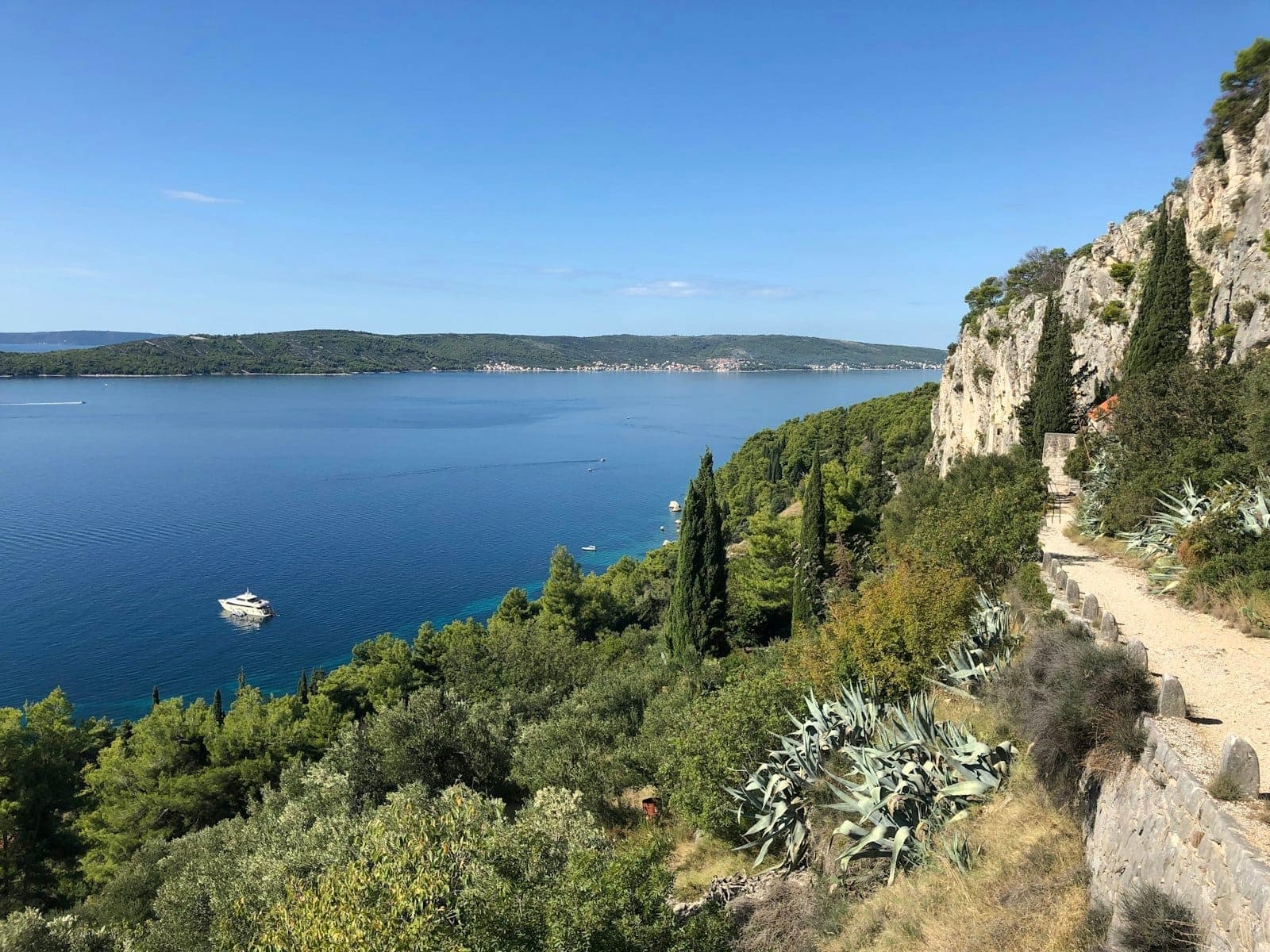 Suggestivo sentiero costiero a Spalato con acqua azzurra limpida, lussureggiante vegetazione e scogliere rocciose sotto un cielo soleggiato.