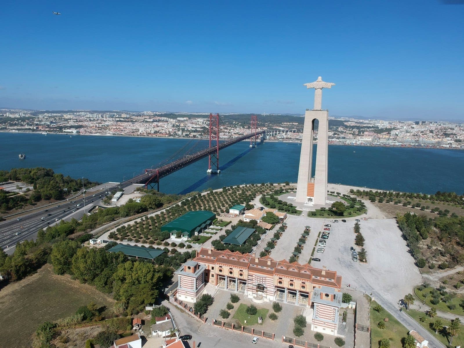 Vista aérea da estátua do Cristo Rei de Lisboa e panorama da cidade com a Ponte 25 de Abril e o rio Tejo num dia limpo.