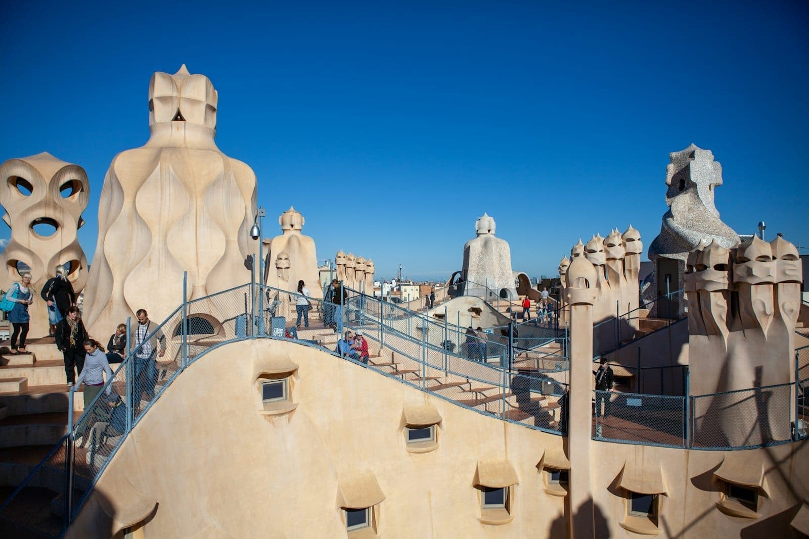 Wide view of Gaudí’s Casa Milà rooftop in Barcelona with sculptural chimneys, blue sky, and visitors exploring the architectural terrace.