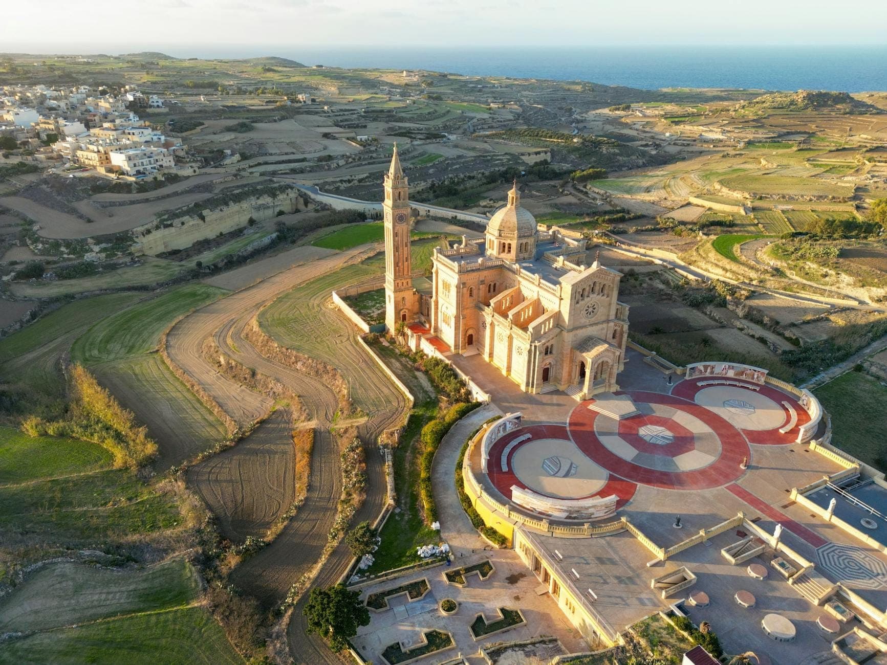มุมมองทางอากาศของมหาวิหาร Ta' Pinu บนเกาะ Gozo พร้อมทุ่งชนบทกว้างใหญ่และทะเลในระยะไกล