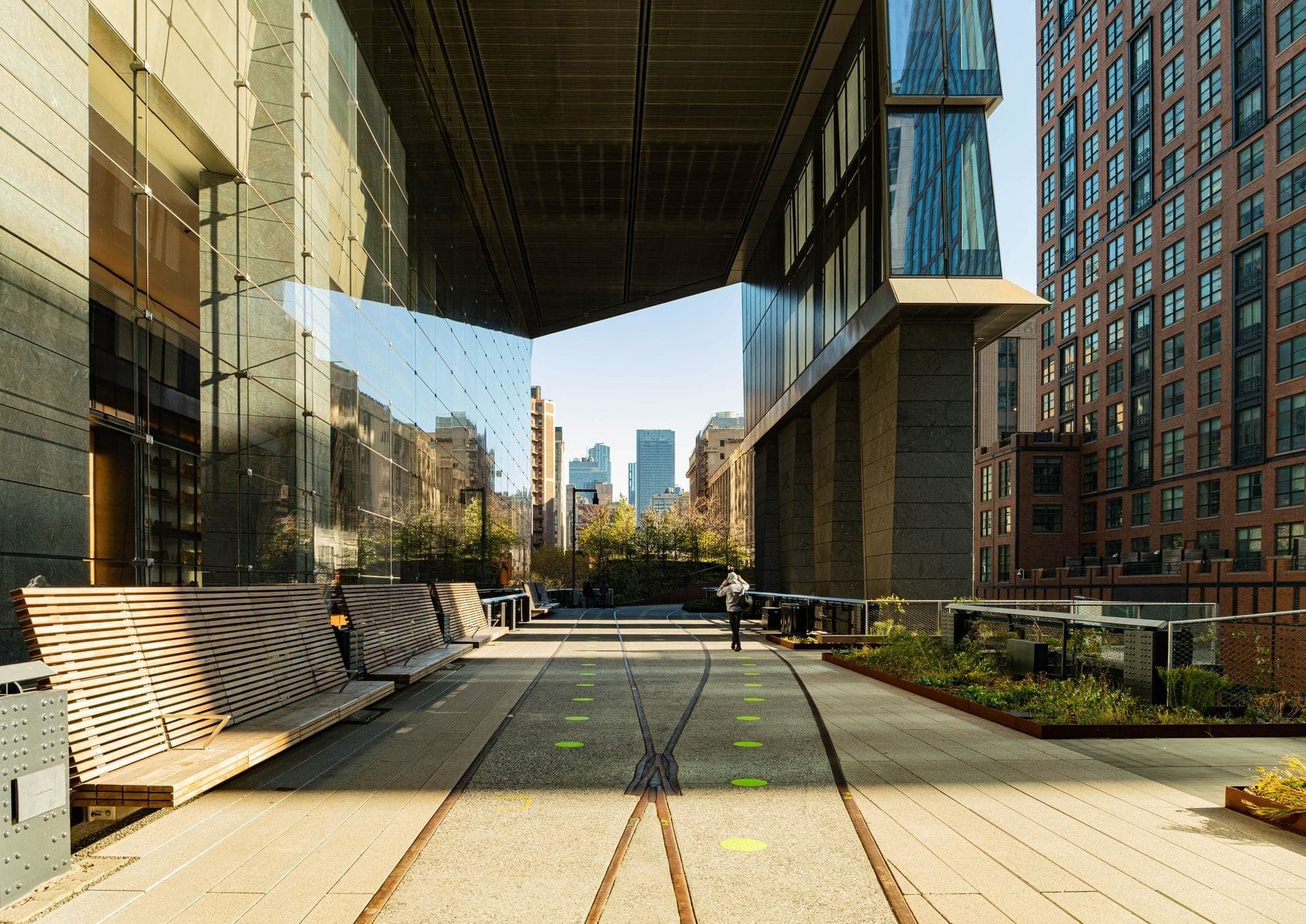 วิวตามแนวสวน High Line ในแมนฮัตตัน พร้อมม้านั่ง ต้นไม้สีเขียว และอาคารสมัยใหม่ที่ล้อมรอบทางเดินยกระดับภายใต้ท้องฟ้าแจ่มใส