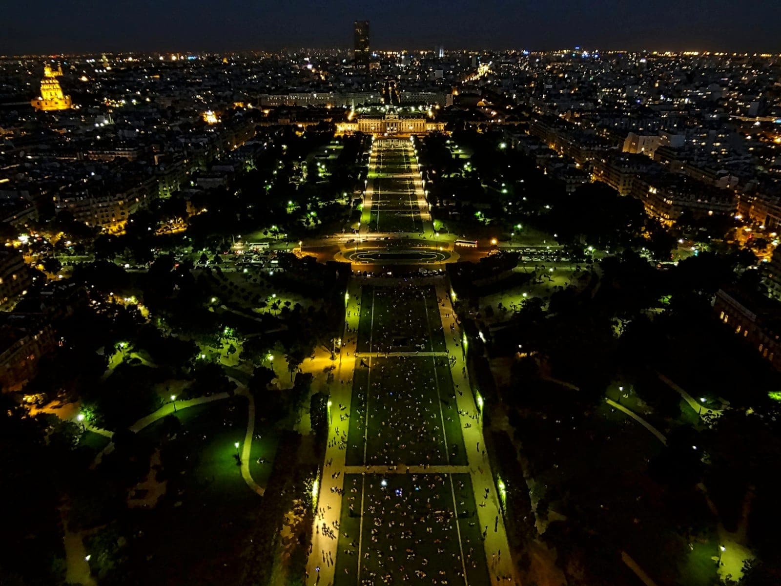 Ночной вид с воздуха на Париж с садами и огнями города, снятый сверху, демонстрирующий классический парижский городской пейзаж.