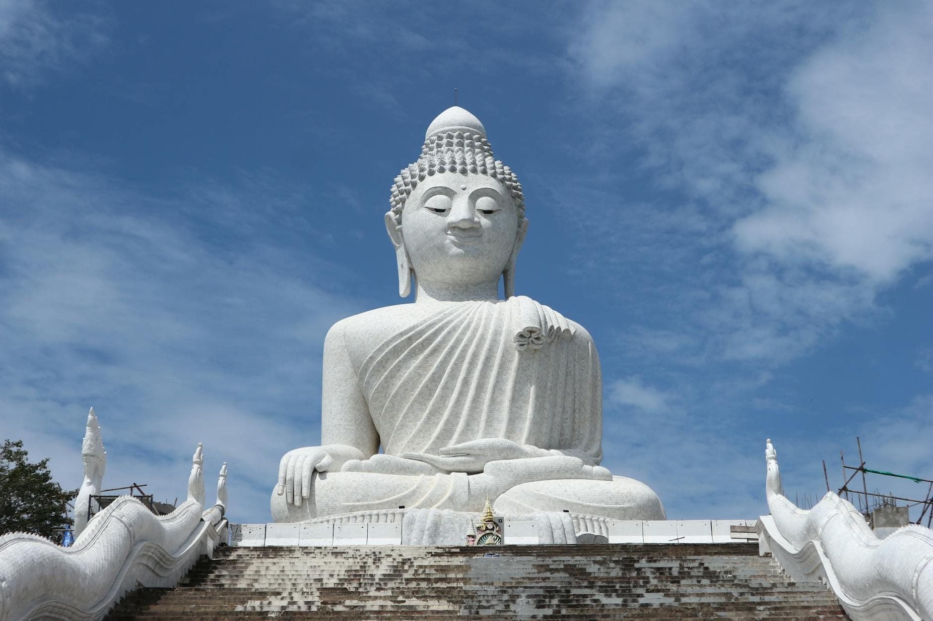 Wide-angle view of the Big Buddha statue seated on a marble platform under a blue sky, with ornate stair railings and majestic presence on Nakkerd Hill.