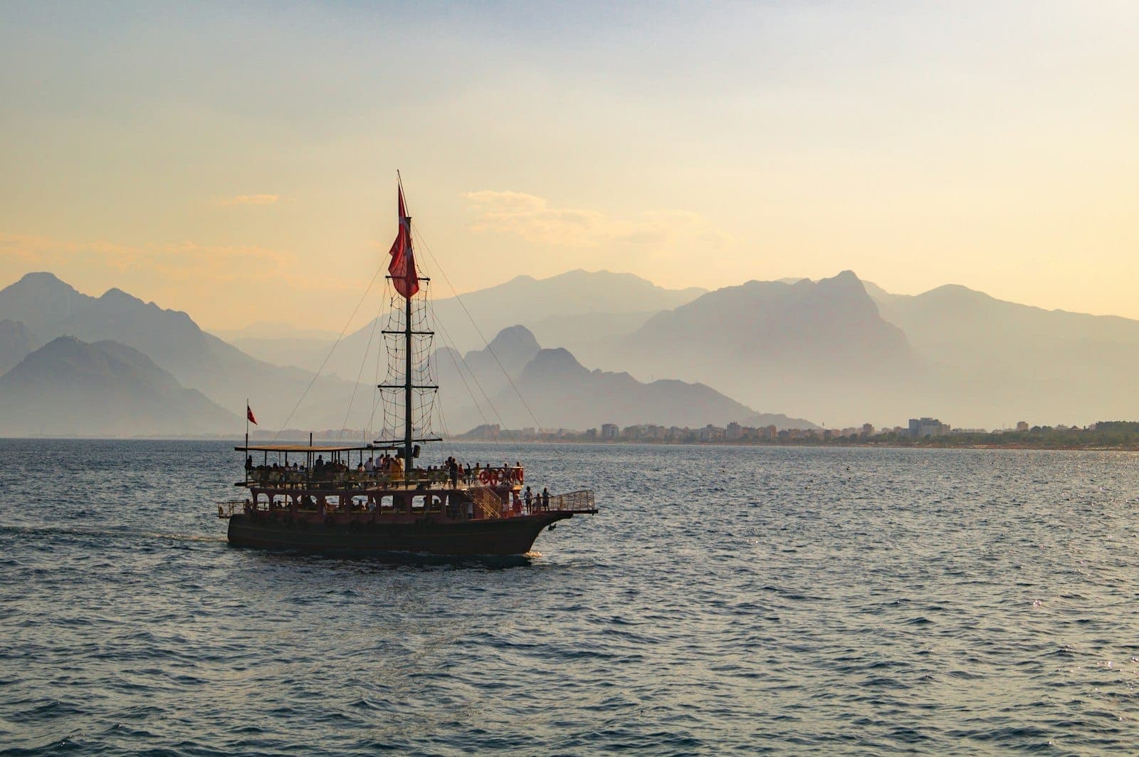Traditionelles Boot auf dem blauen Meer bei Sonnenuntergang, im Hintergrund die zerklüfteten Berge Antalyas unter warmem Abendhimmel.