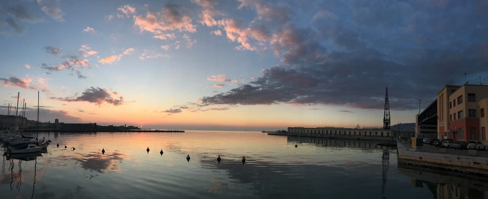 Ampia vista sul lungomare all'alba con mare calmo, piccole barche, edifici del centro storico a destra e il molo Matejuška a Spalato.