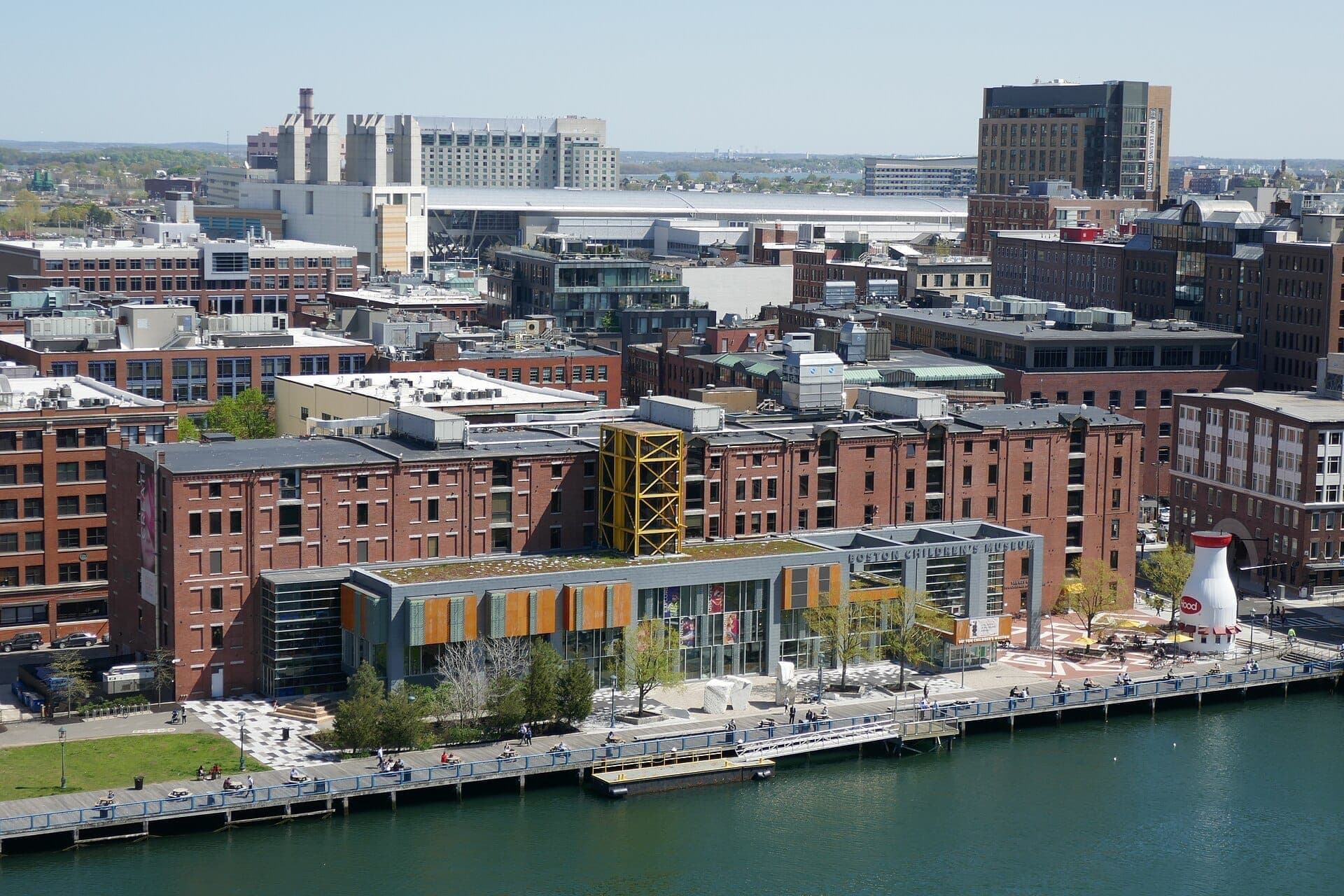 Vue aérienne du Boston Children's Museum avec son entrée en verre moderne, ses bâtiments en briques rouges, sa promenade en bois et le Fort Point Channel en plein jour.