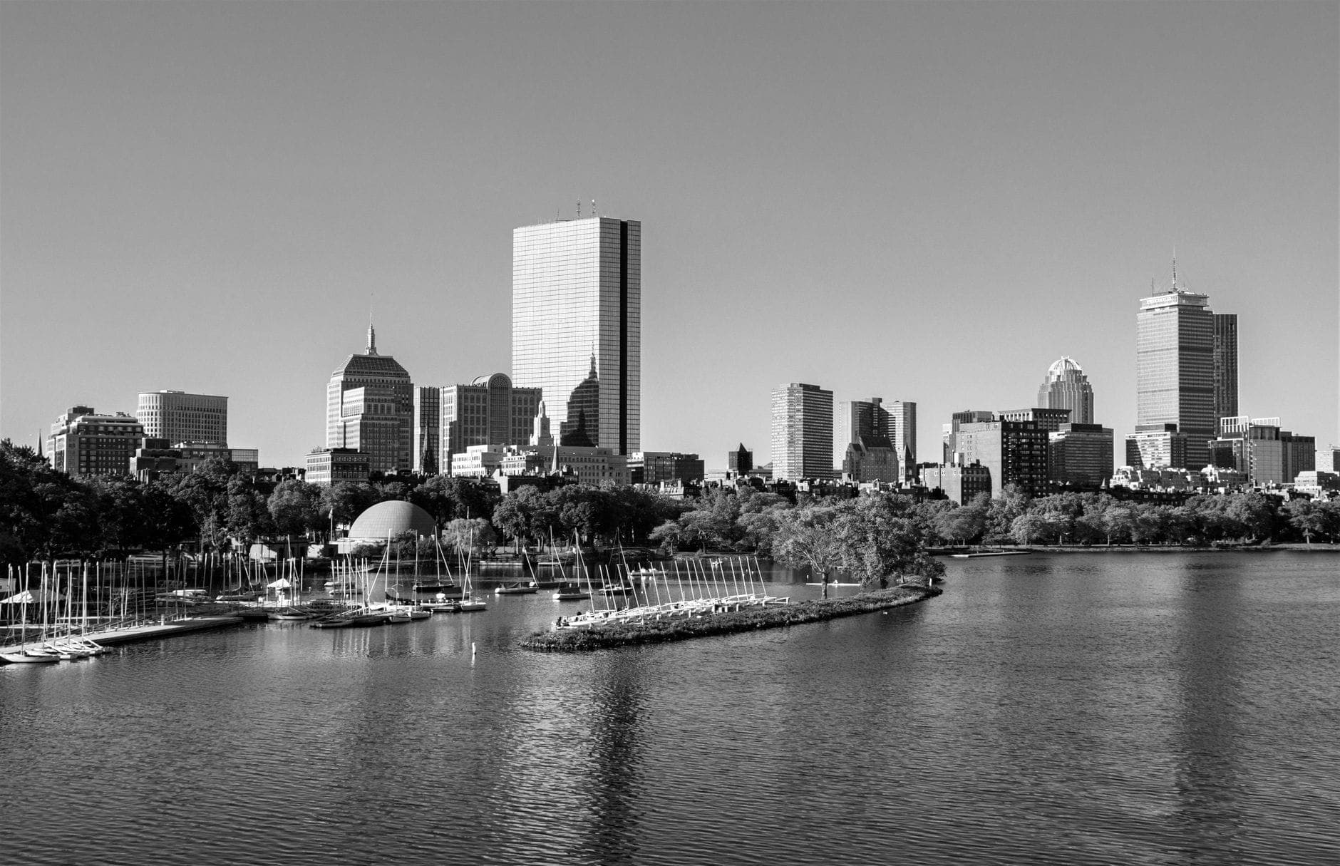 Photo en noir et blanc de la skyline de Boston vue depuis la Charles River, avec l'Esplanade Hatch Shell et des voiliers.