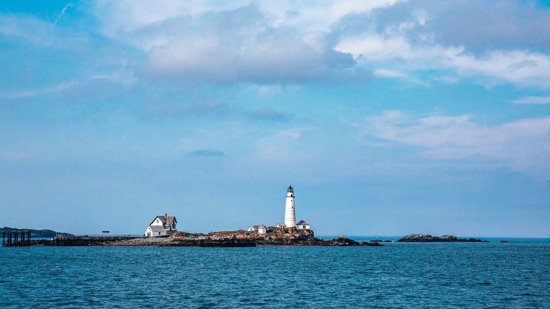 Vue panoramique sur Boston Harbor avec le phare historique et la maison du gardien sur un petit îlot rocheux sous un ciel bleu.