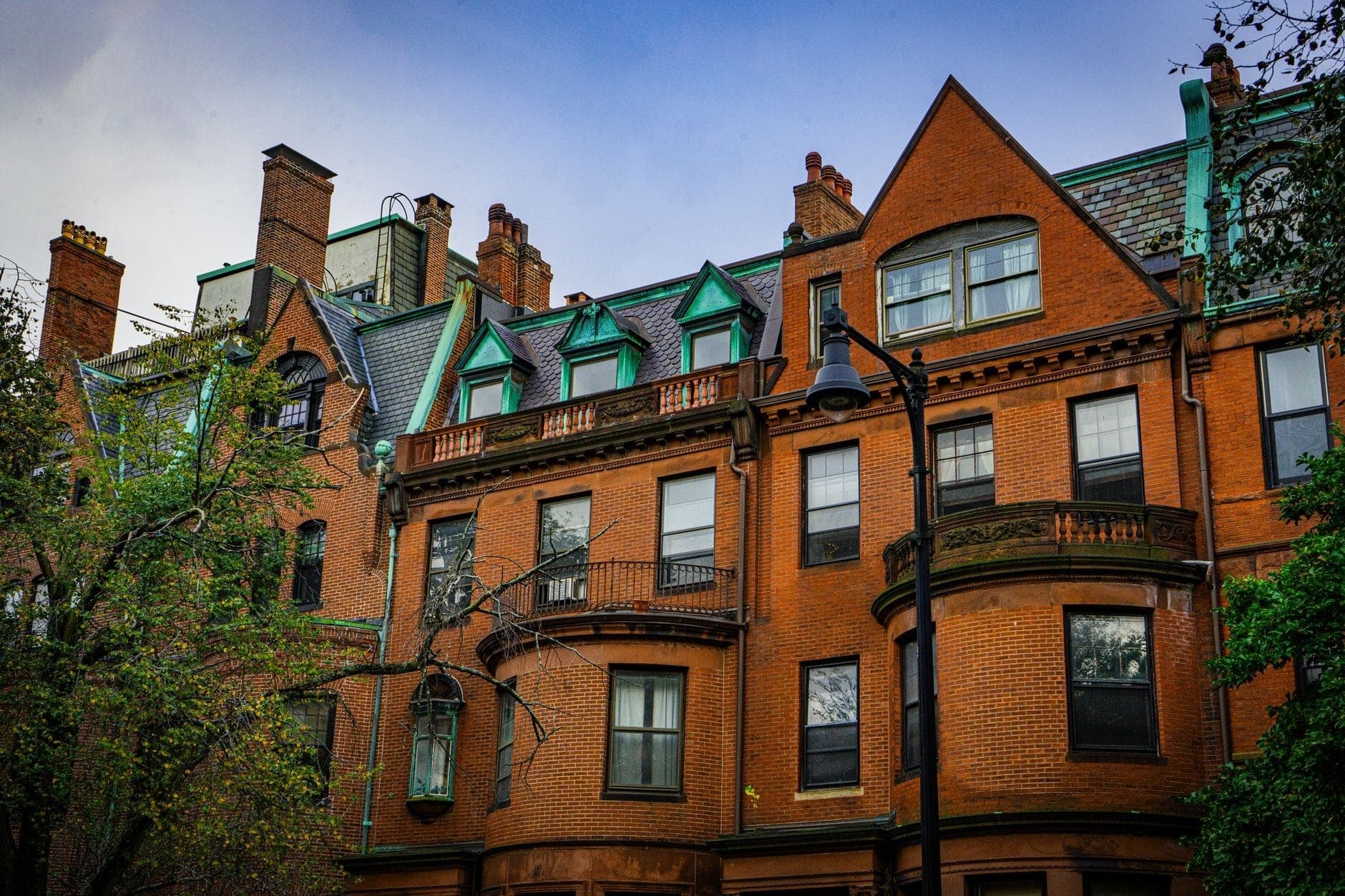 Maisons en rangée en brique distinctives avec bow-windows et toitures ornementées dans le quartier historique de Back Bay à Boston, encadrées par des arbres et un lampadaire.