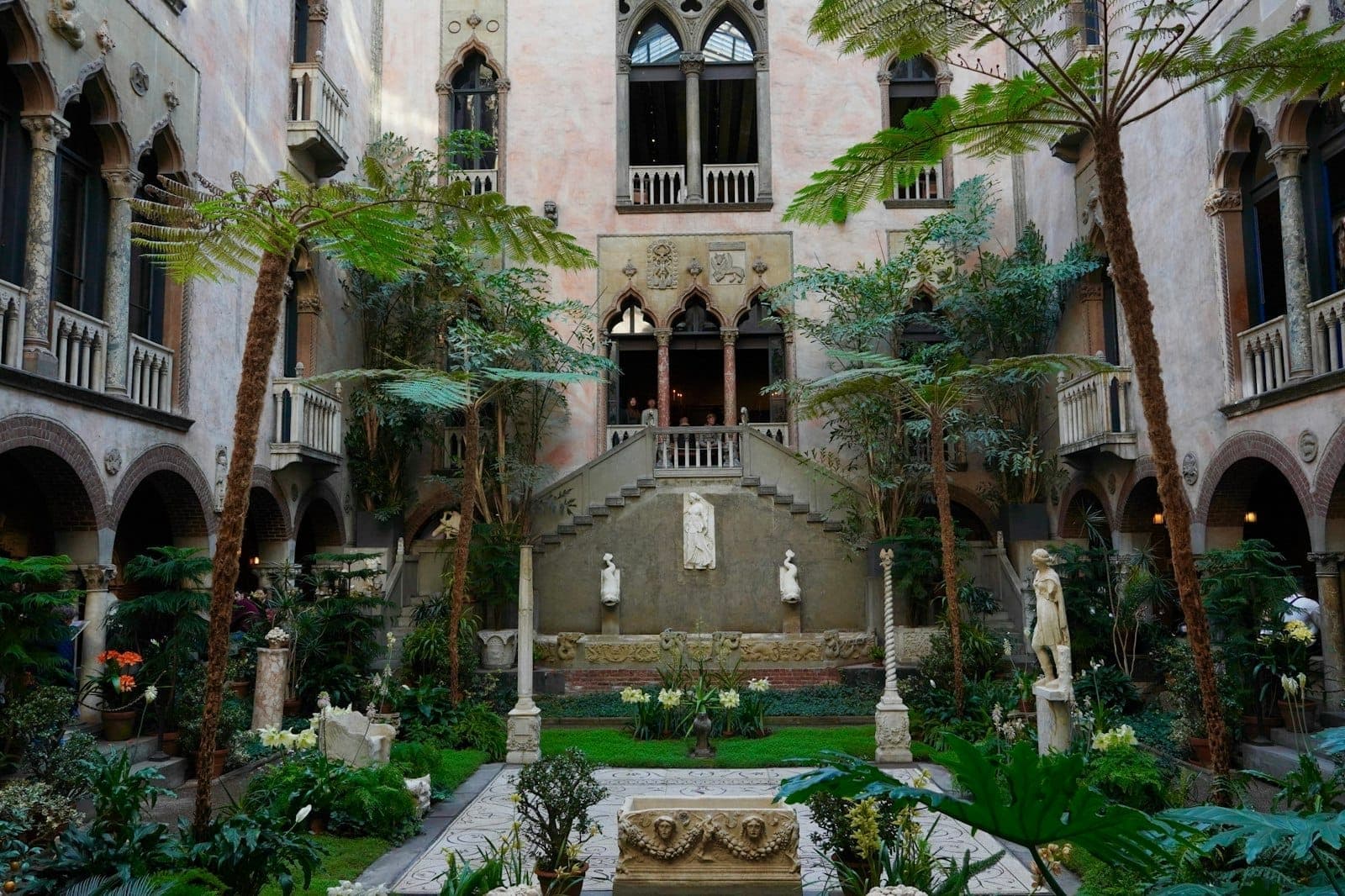 Vue large d'une cour intérieure ornée avec des fenêtres en arc, des sculptures et des plantes luxuriantes dans un musée historique de Boston.
