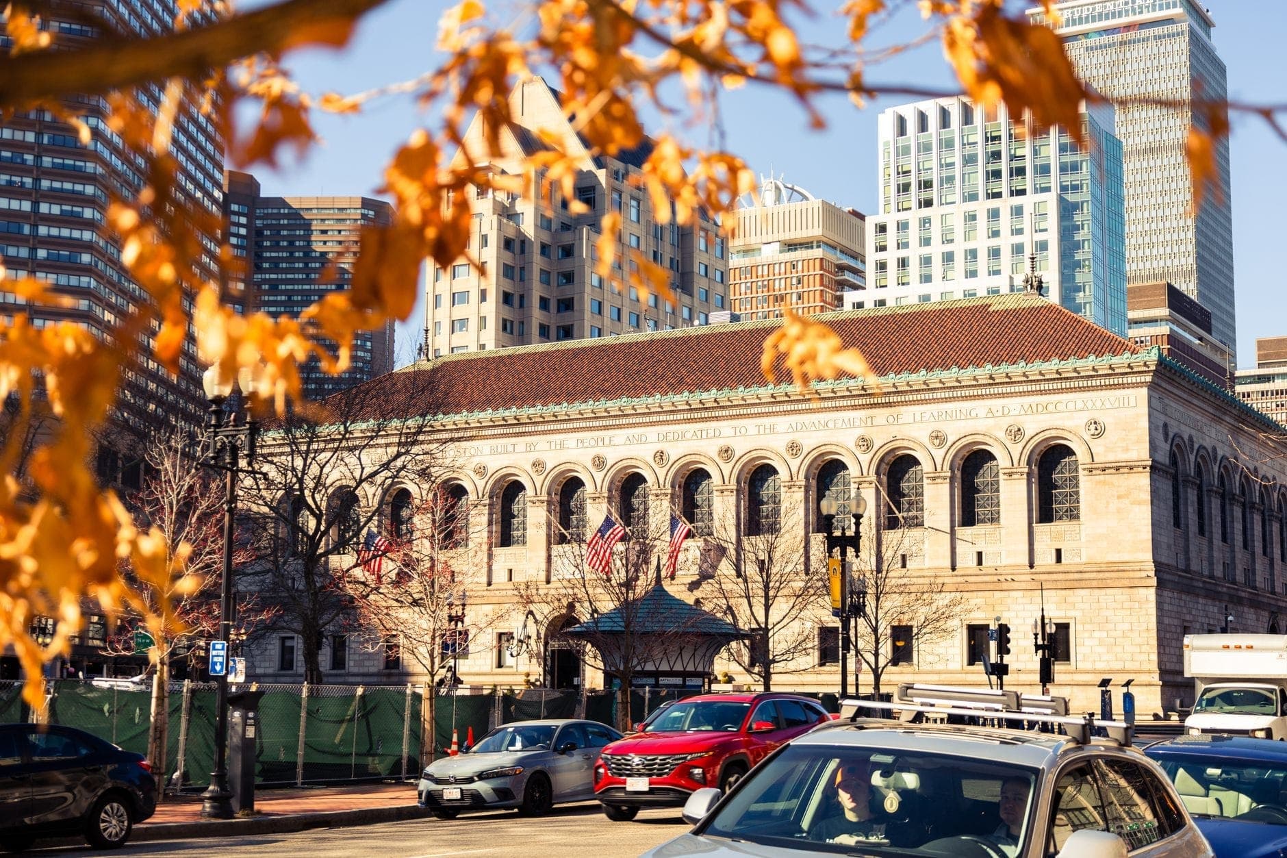 Boston Public Library et immeubles de la ville avec des feuilles d'automne et des voitures au premier plan, capturant l'atmosphère de l'automne à Boston.