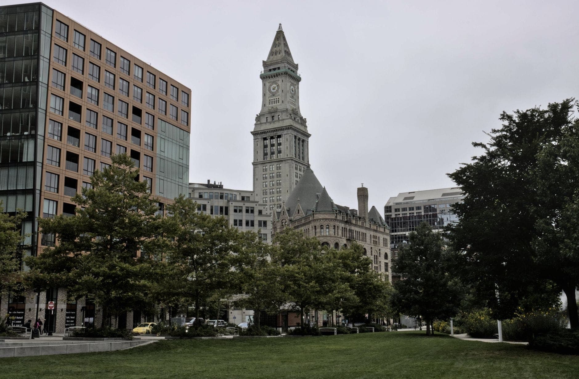 La Custom House Tower de Boston se dressant derrière un espace vert et des bâtiments modernes, sous un ciel nuageux dans le centre-ville de Boston.
