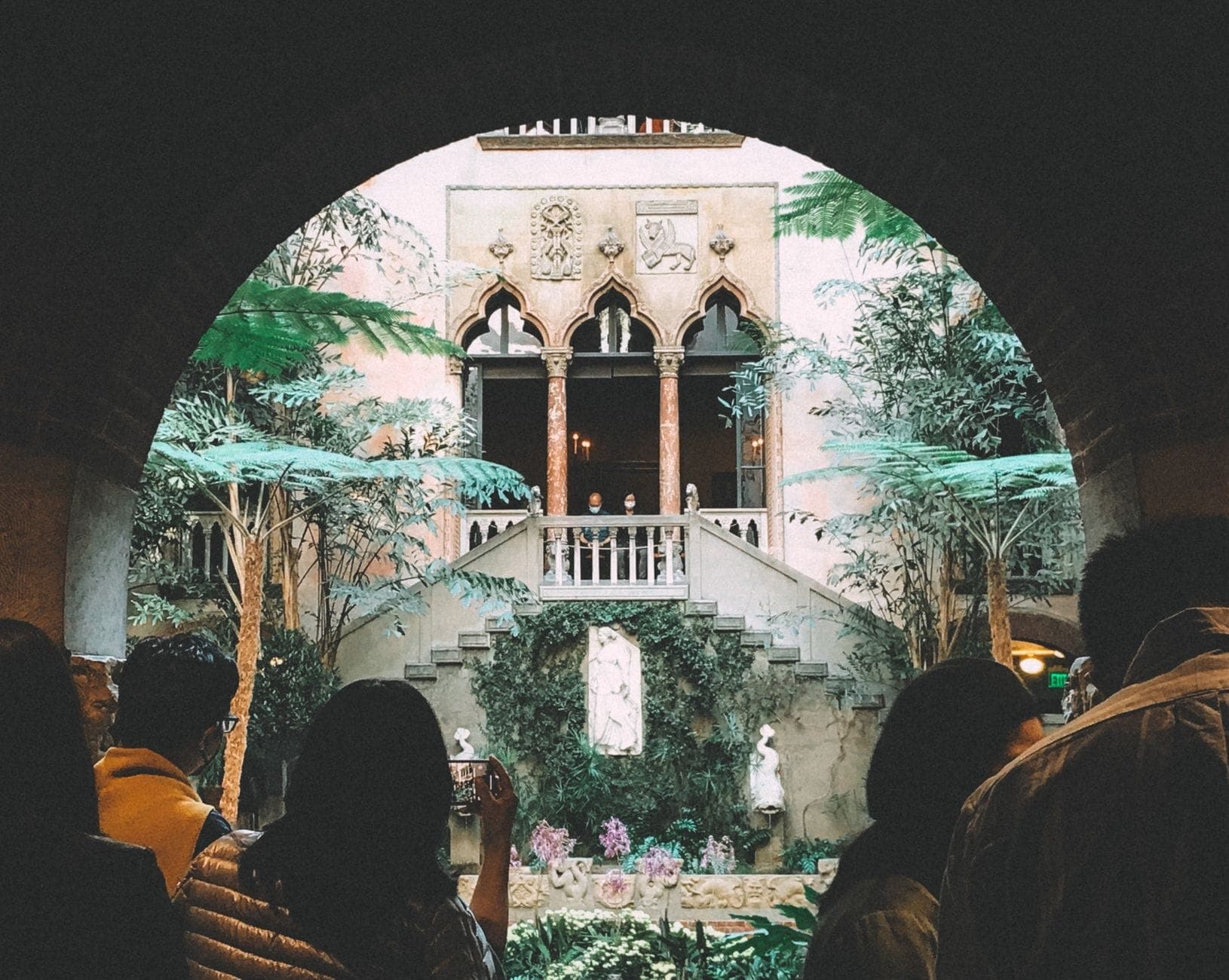 Des visiteurs se tiennent sous une arche et regardent le jardin intérieur de l'Isabella Stewart Gardner Museum à Boston.