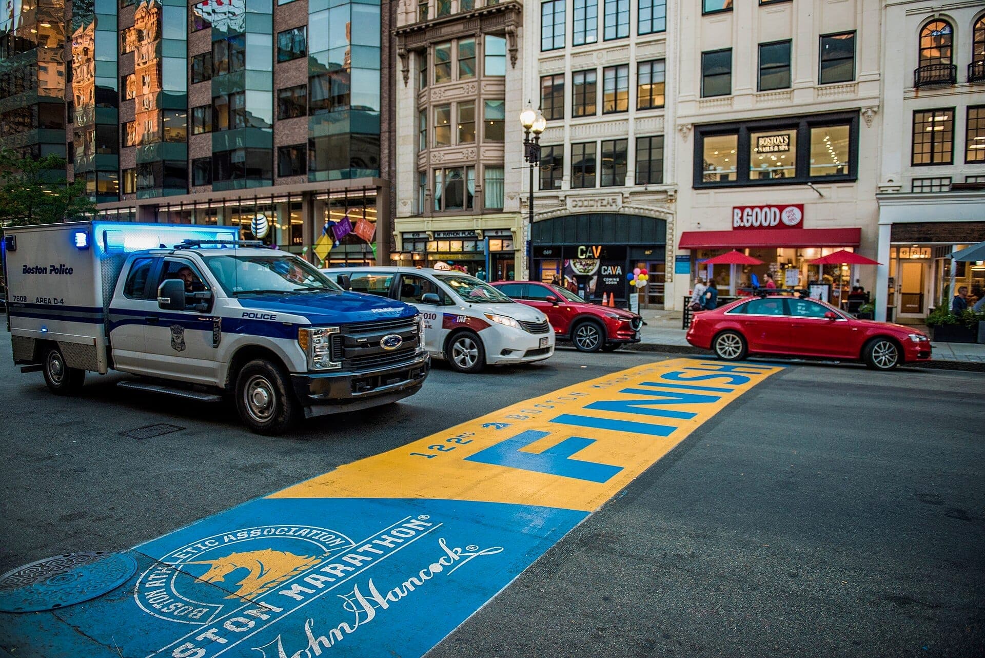 Ligne d'arrivée du Boston Marathon sur Boylston Street, marquée en bleu et jaune, avec des voitures garées et des bâtiments environnants en arrière-plan.