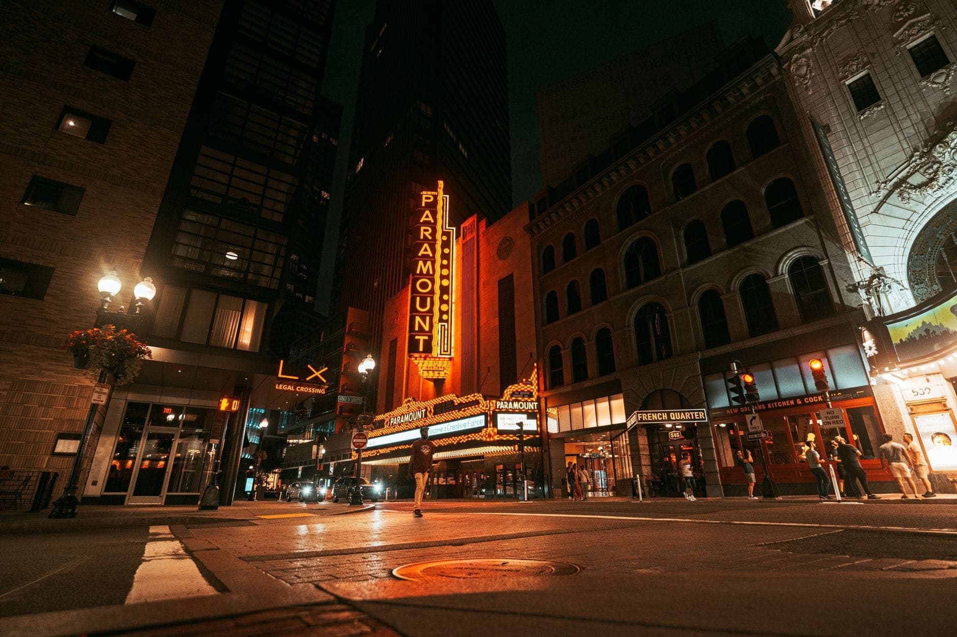 Le centre de Boston de nuit, avec des enseignes lumineuses, des bâtiments historiques et des passants devant le Paramount Theatre — l'énergie nocturne de la ville en pleine effervescence.