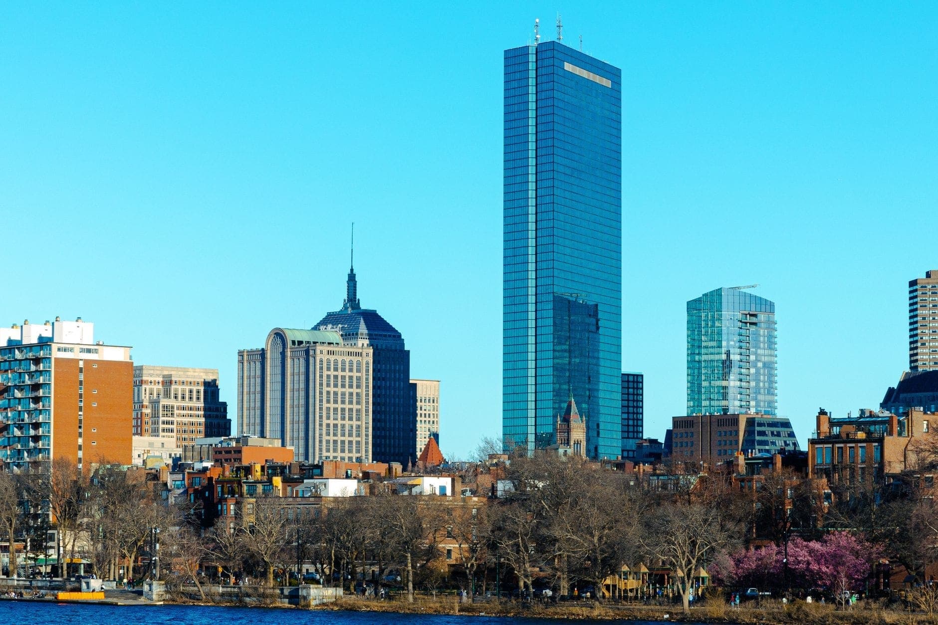 Vue lumineuse et dégagée de la skyline de Boston avec des gratte-ciel imposants et des arbres dénudés le long de la Charles River par une journée fraîche.